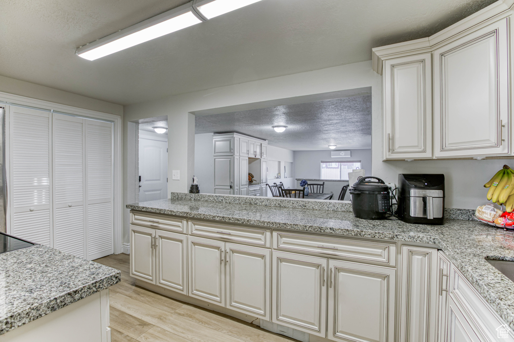 Kitchen with kitchen peninsula, a textured ceiling, light hardwood / wood-style floors, and light stone counters