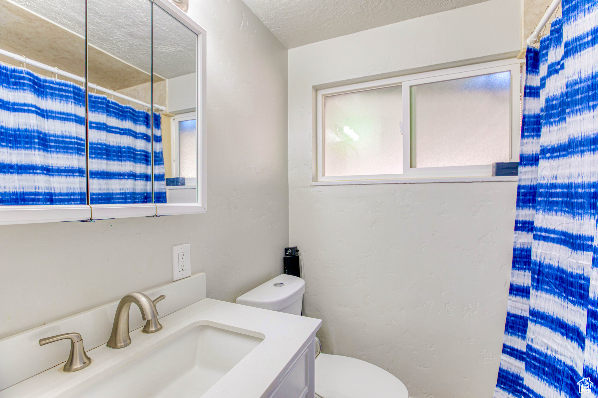 Bathroom featuring a shower with curtain, vanity, toilet, and a textured ceiling