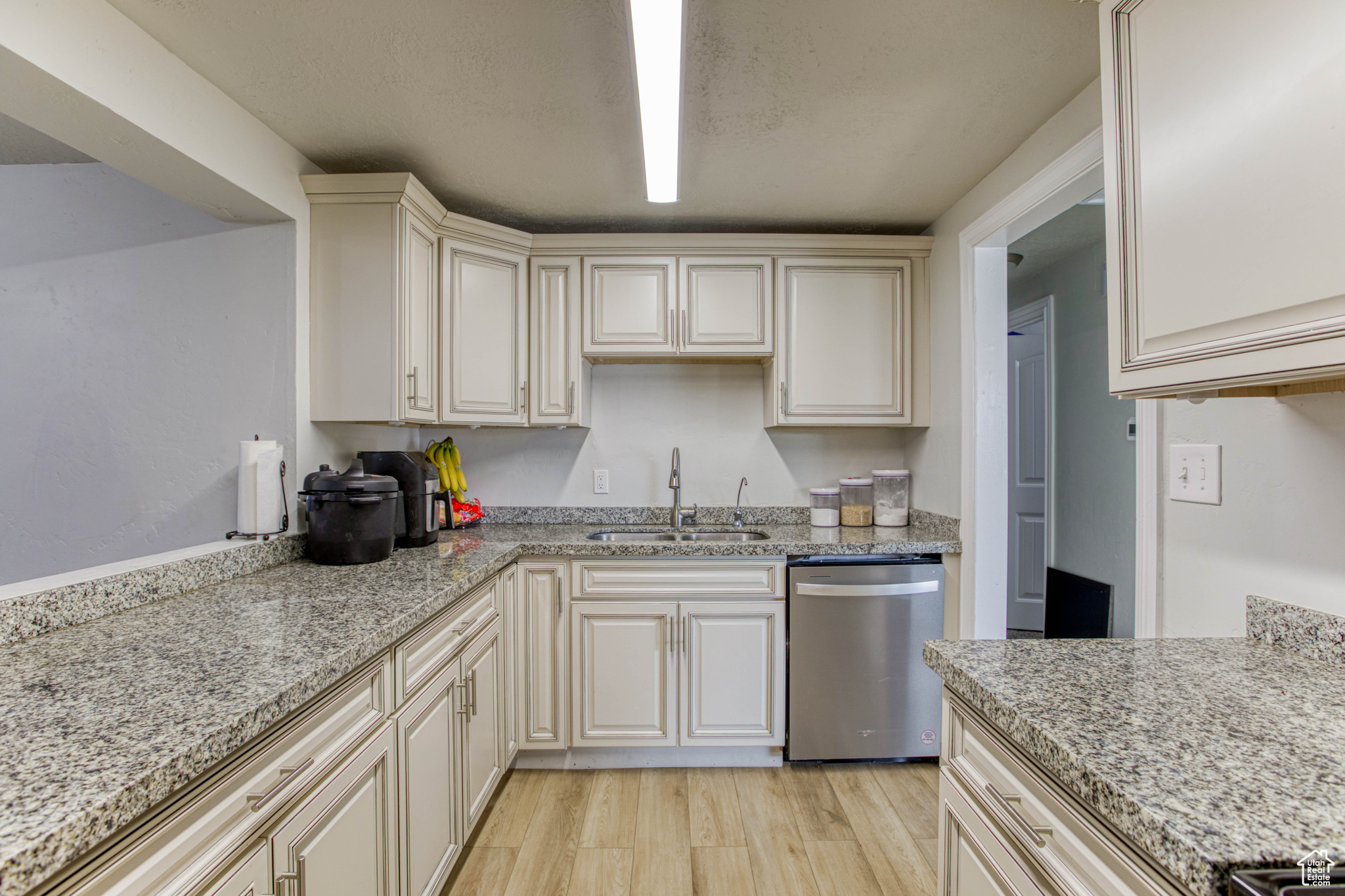 Kitchen with dishwasher, cream cabinets, sink, light stone countertops, and light hardwood / wood-style floors