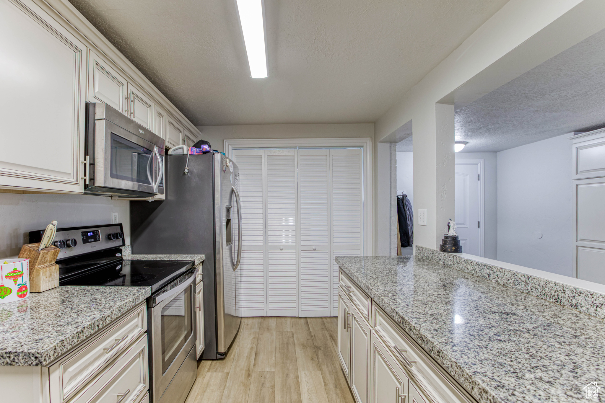 Kitchen featuring light stone countertops, light wood-type flooring, a textured ceiling, and appliances with stainless steel finishes