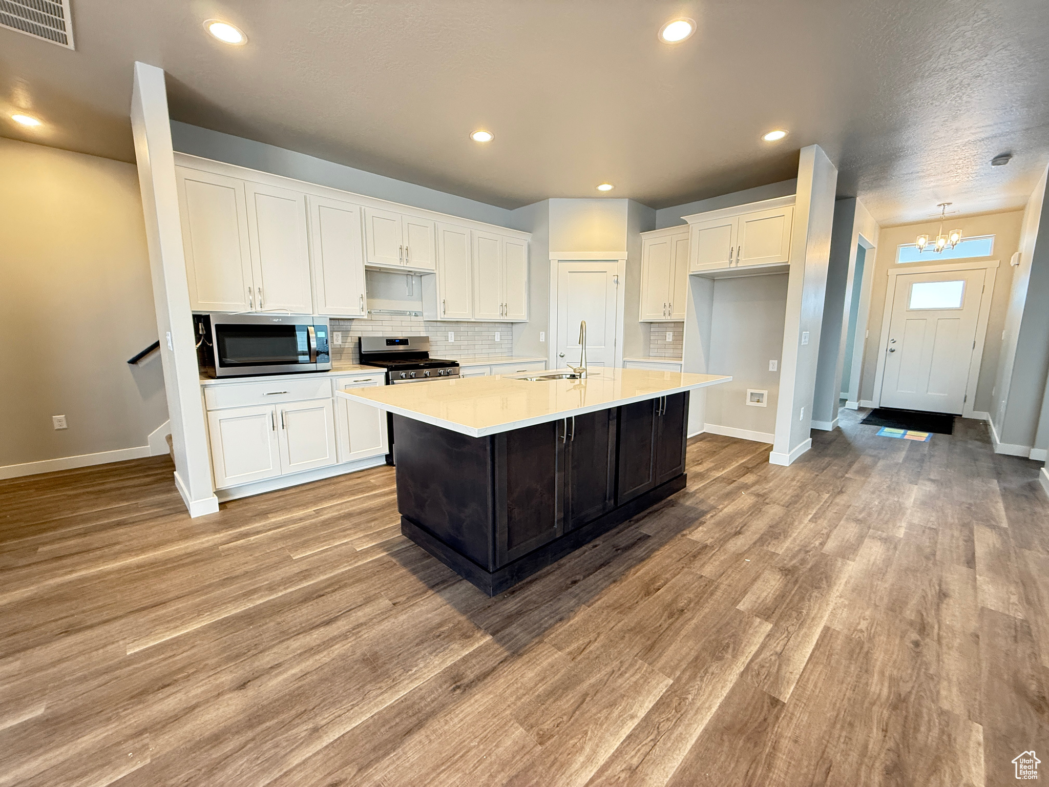 Kitchen featuring appliances with stainless steel finishes, tasteful backsplash, white cabinetry, a center island with sink, and light wood-type flooring