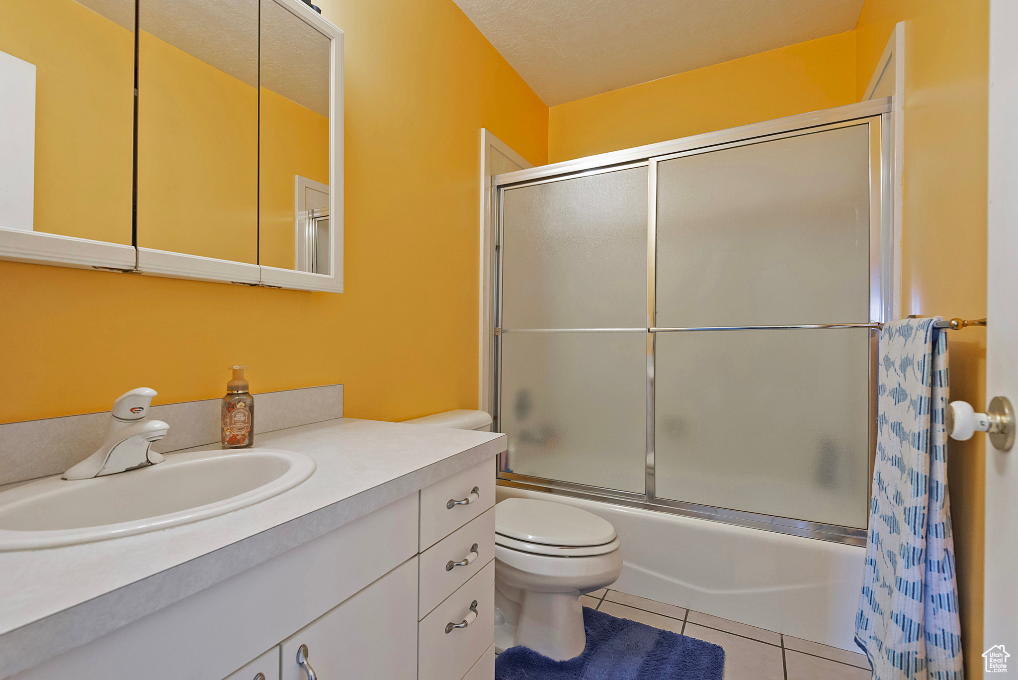 Full bathroom with combined bath / shower with glass door, vanity, tile patterned floors, and toilet