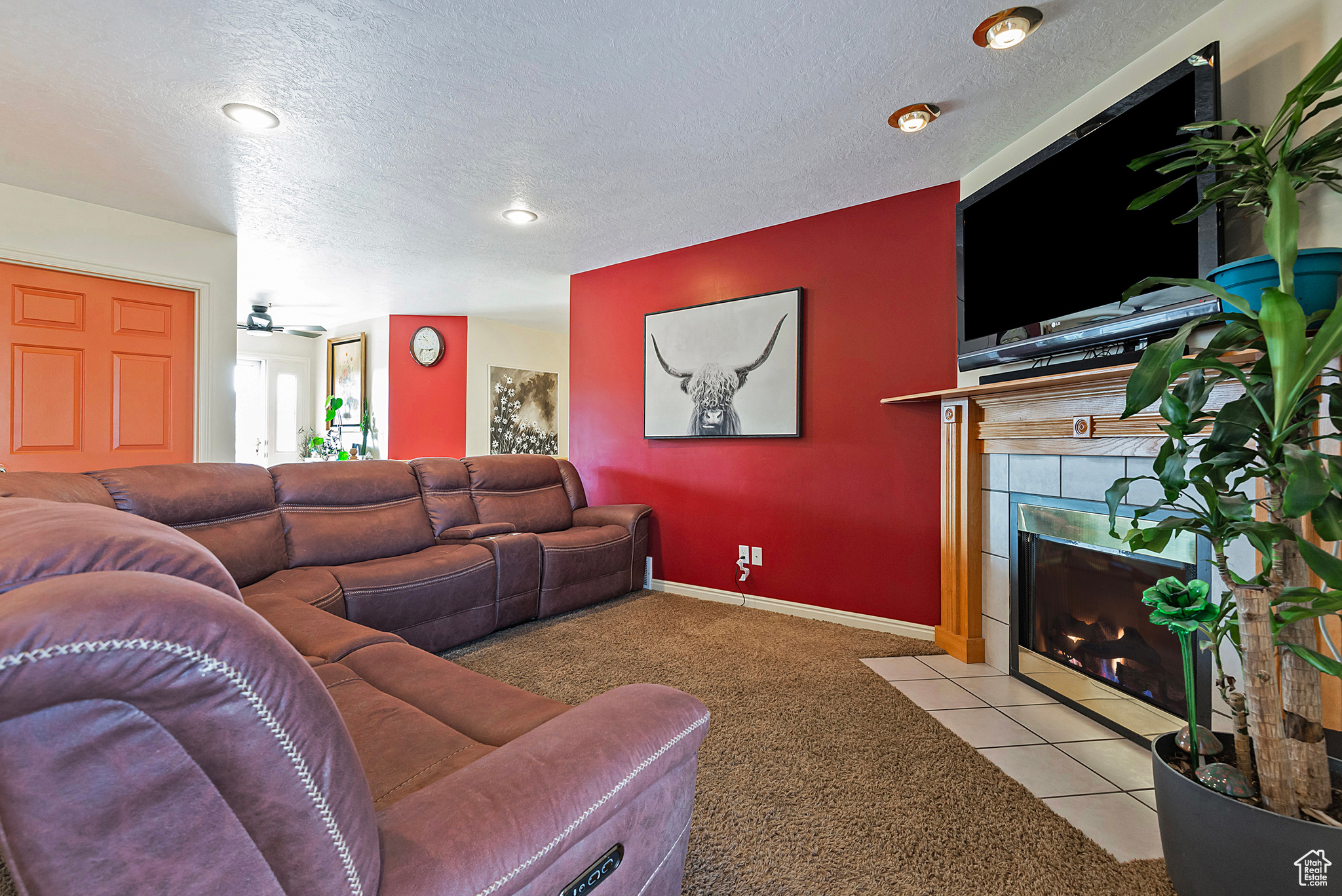 Carpeted living room with a textured ceiling, ceiling fan, and a fireplace