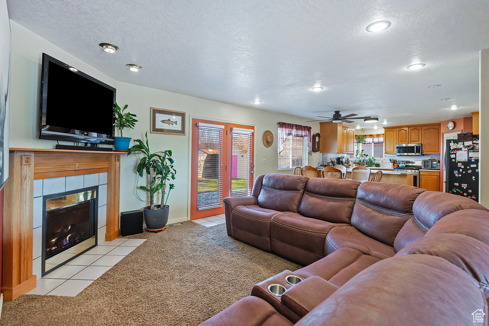 Carpeted living room with ceiling fan, a textured ceiling, and a tiled fireplace