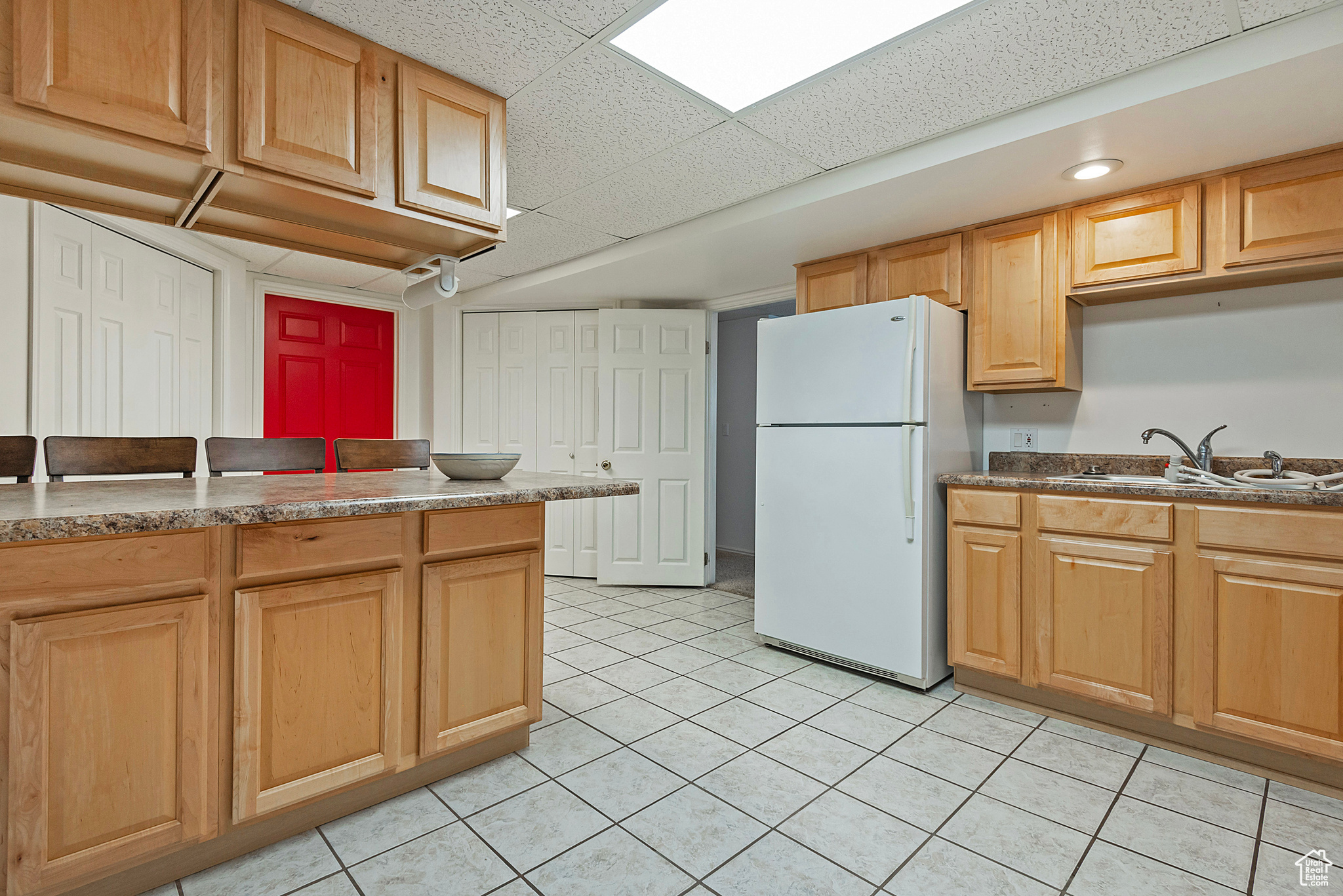 Kitchen with a paneled ceiling, white refrigerator, light tile patterned flooring, and sink