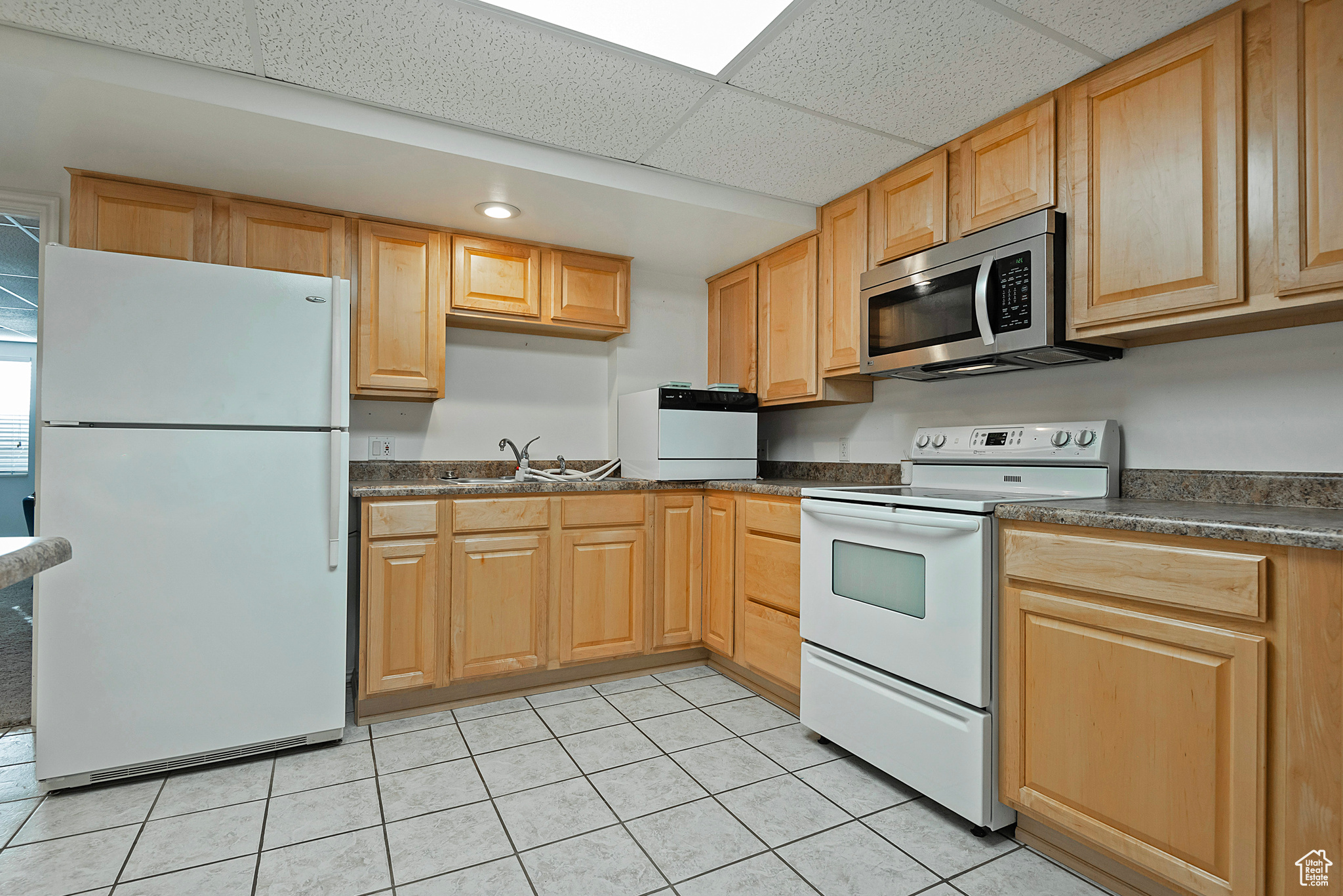 Kitchen featuring a drop ceiling, white appliances, sink, and light tile patterned floors