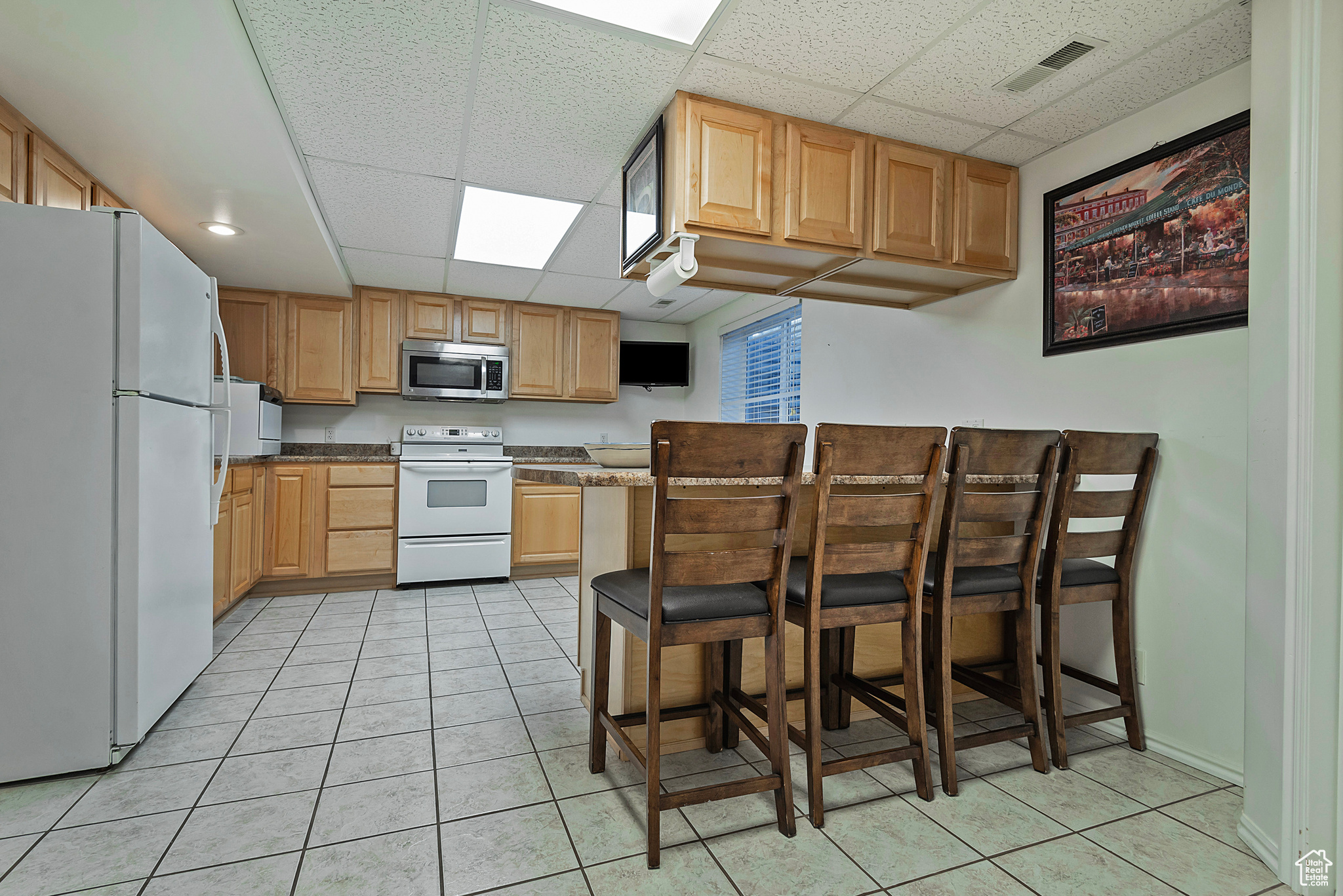 Kitchen with a paneled ceiling, dark stone countertops, light tile patterned floors, and white appliances