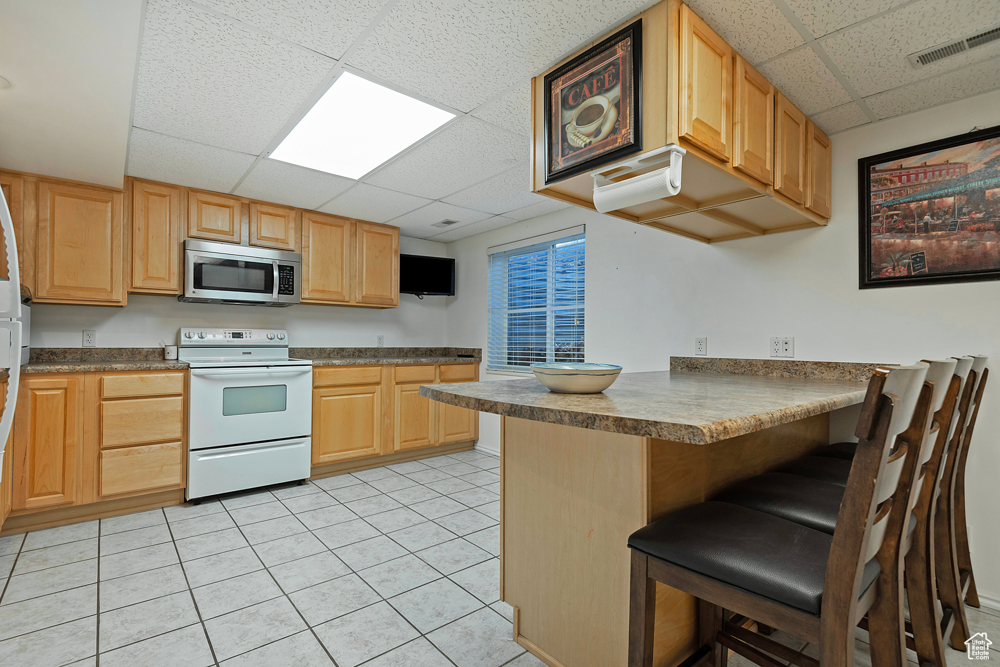 Kitchen with kitchen peninsula, a paneled ceiling, white electric stove, and a breakfast bar area