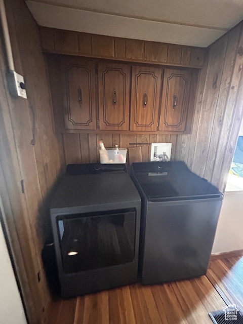 Washroom featuring cabinets, wood walls, wood-type flooring, and separate washer and dryer