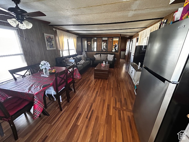 Dining area with a textured ceiling, dark hardwood / wood-style floors, ceiling fan, and wood walls