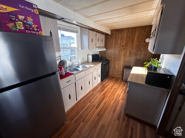 Kitchen with stainless steel fridge, dark hardwood / wood-style flooring, black range with gas stovetop, white cabinetry, and wood walls