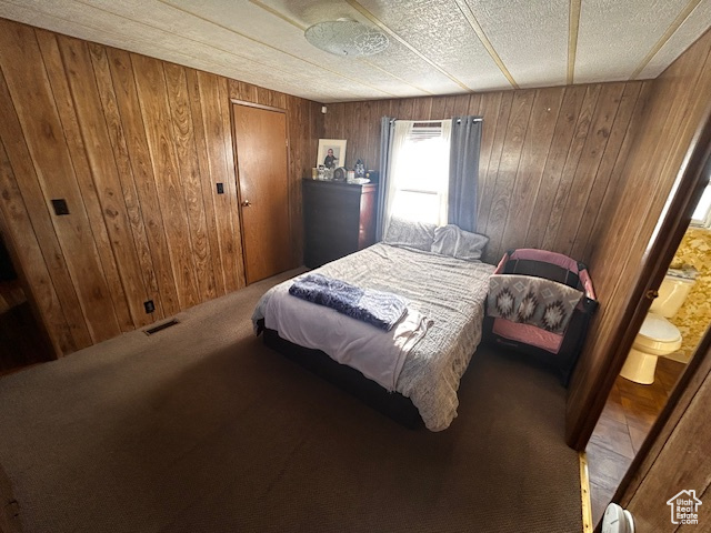 Bedroom with dark colored carpet, a textured ceiling, ensuite bath, and wood walls