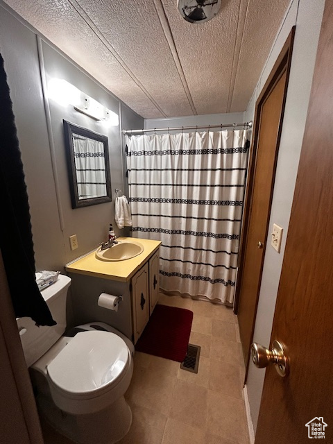 Bathroom with vanity, curtained shower, toilet, and a textured ceiling