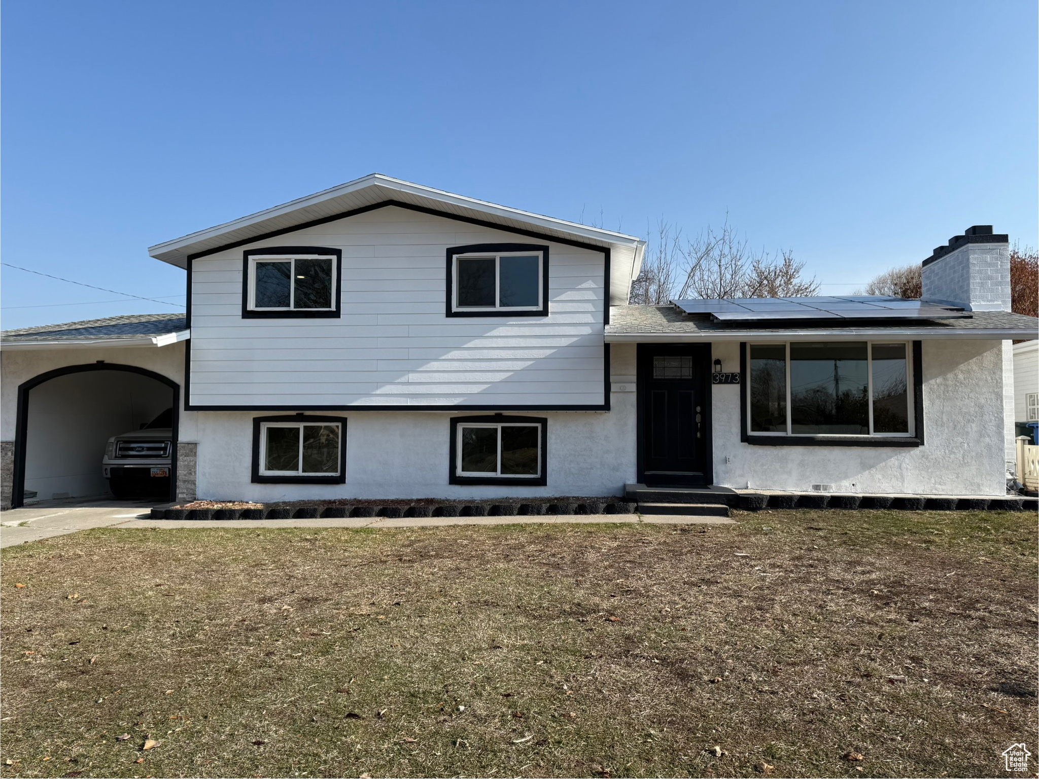 Tri-level home featuring solar panels, a front yard, and a carport