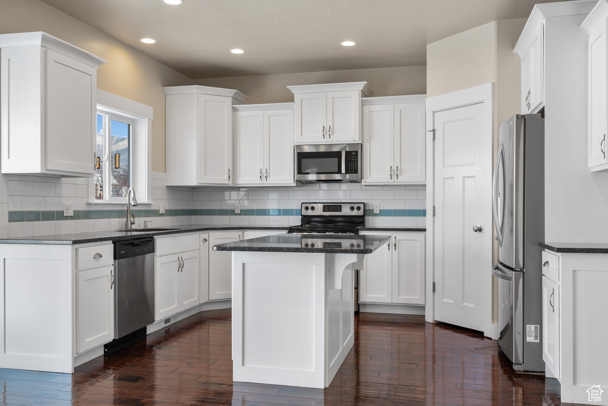 Kitchen with appliances with stainless steel finishes, sink, white cabinets, backsplash, and a center island