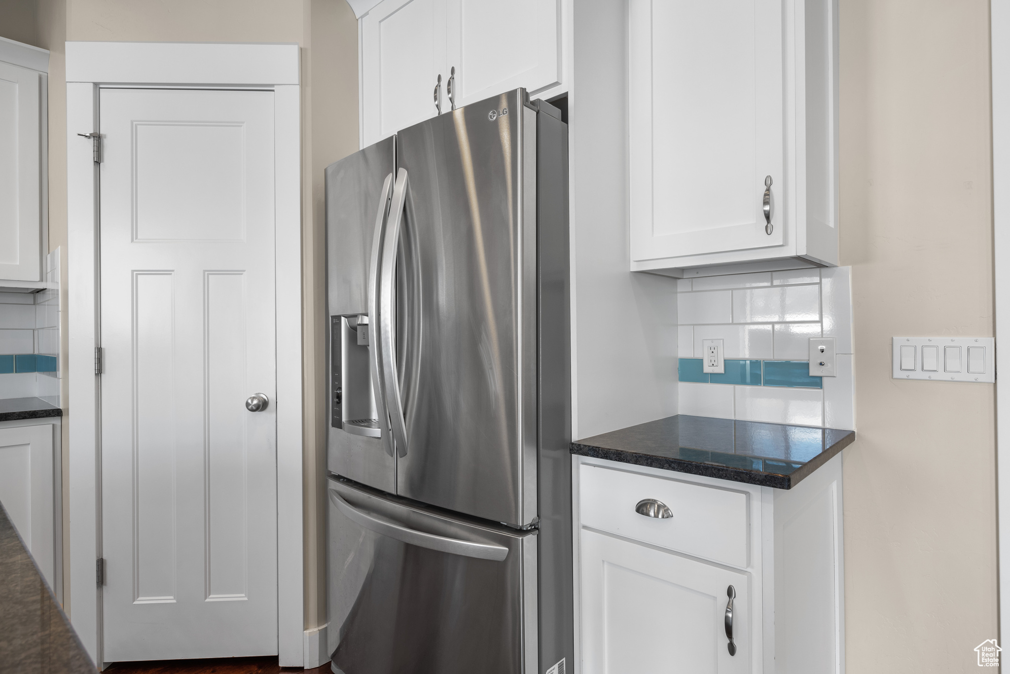 Kitchen with dark stone countertops, stainless steel fridge with ice dispenser, backsplash, and white cabinets