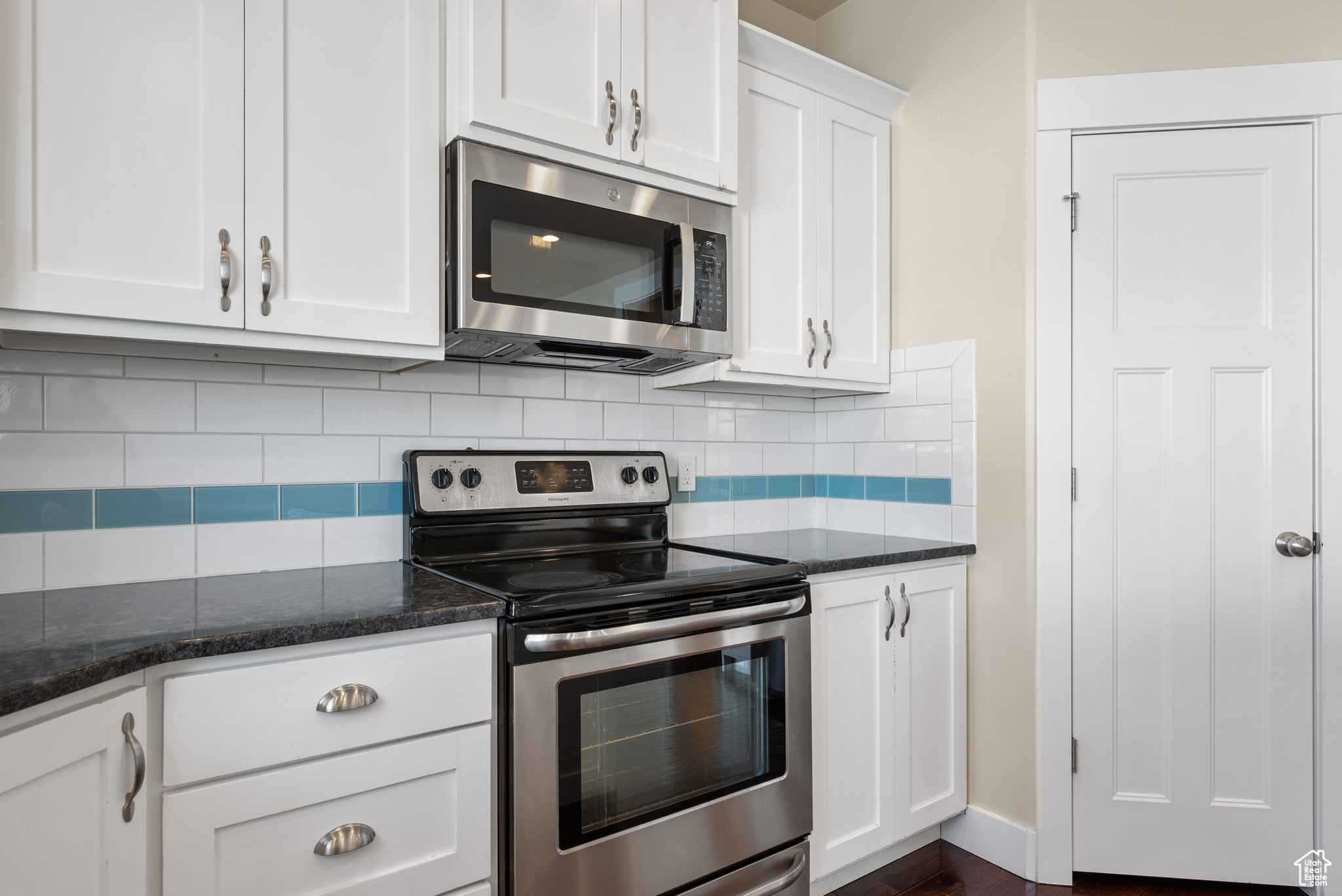 Kitchen featuring tasteful backsplash, appliances with stainless steel finishes, white cabinets, and dark stone counters