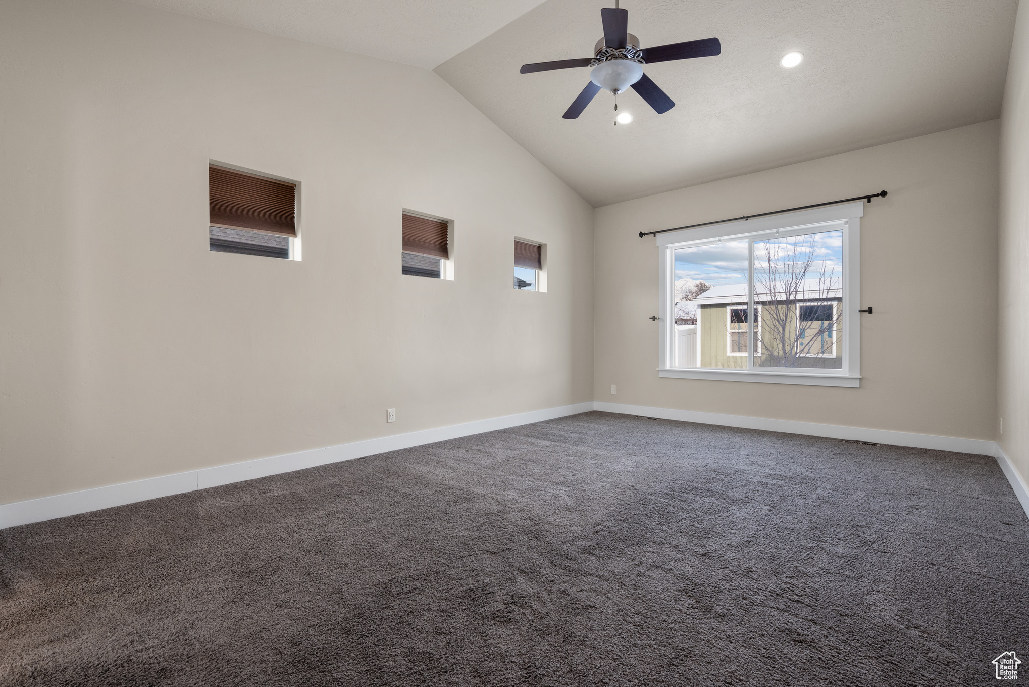 Unfurnished room with ceiling fan, vaulted ceiling, and dark colored carpet