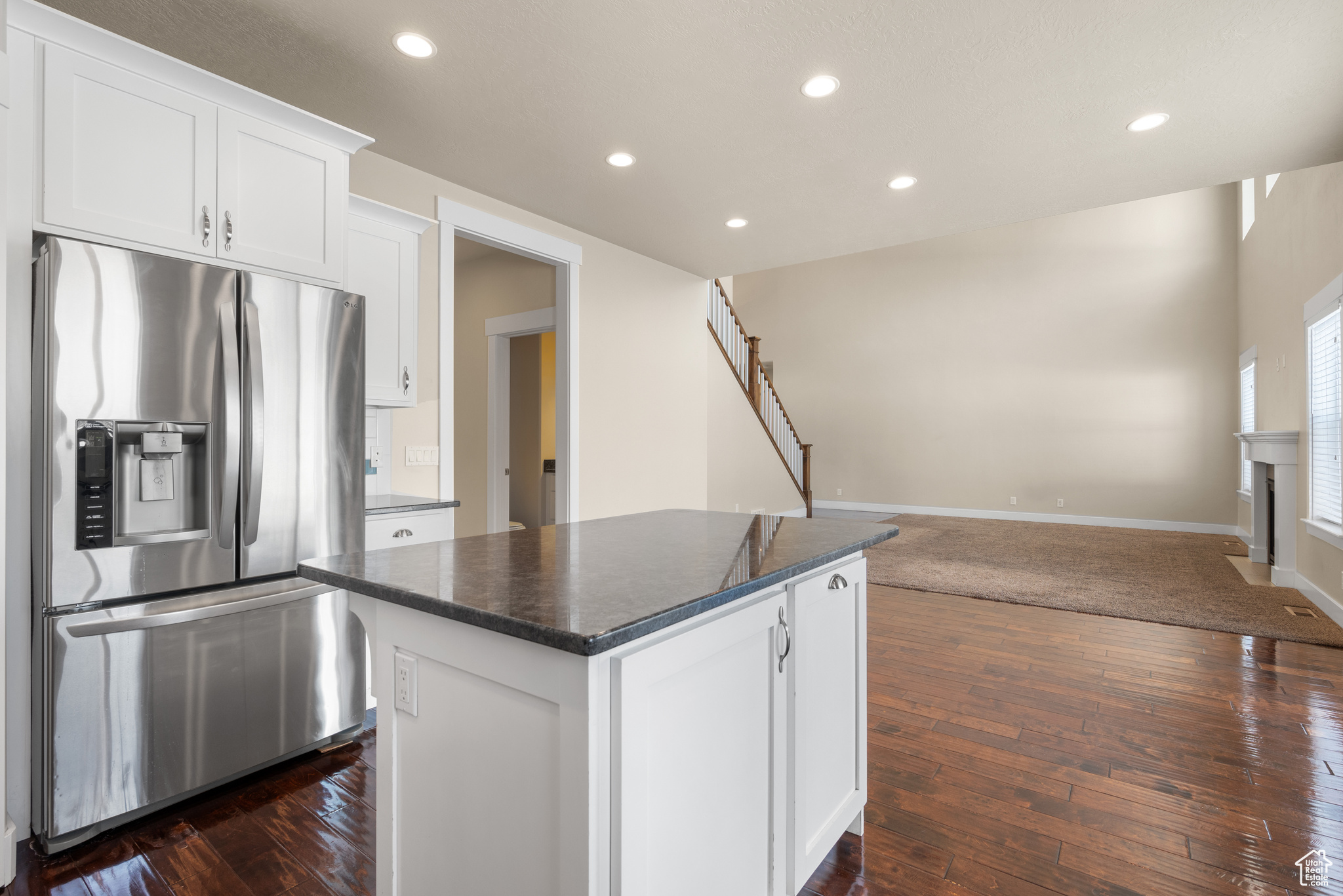 Kitchen featuring a kitchen island, white cabinetry, stainless steel fridge, dark stone counters, and dark wood-type flooring