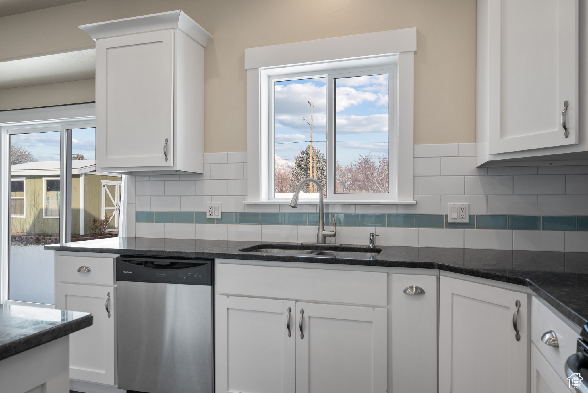 Kitchen with white cabinetry, sink, stainless steel dishwasher, and a healthy amount of sunlight