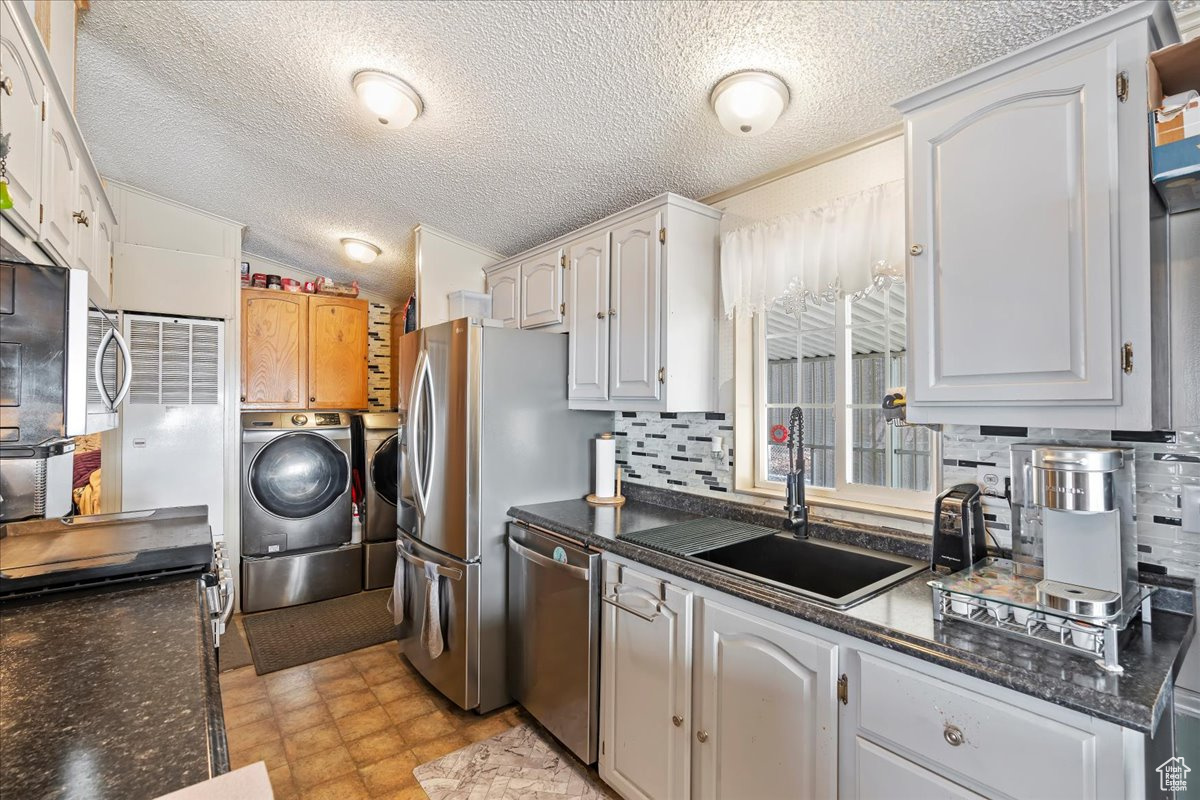 Kitchen with white cabinets, sink, independent washer and dryer, appliances with stainless steel finishes, and tasteful backsplash