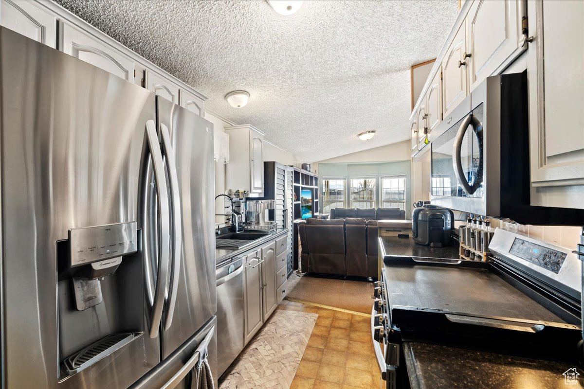 Kitchen with white cabinetry, sink, stainless steel appliances, a textured ceiling, and lofted ceiling