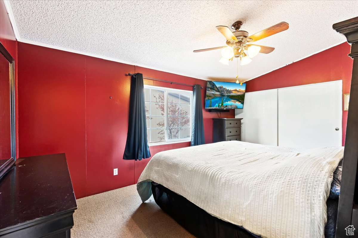 Bedroom with carpet flooring, ceiling fan, lofted ceiling, and a textured ceiling