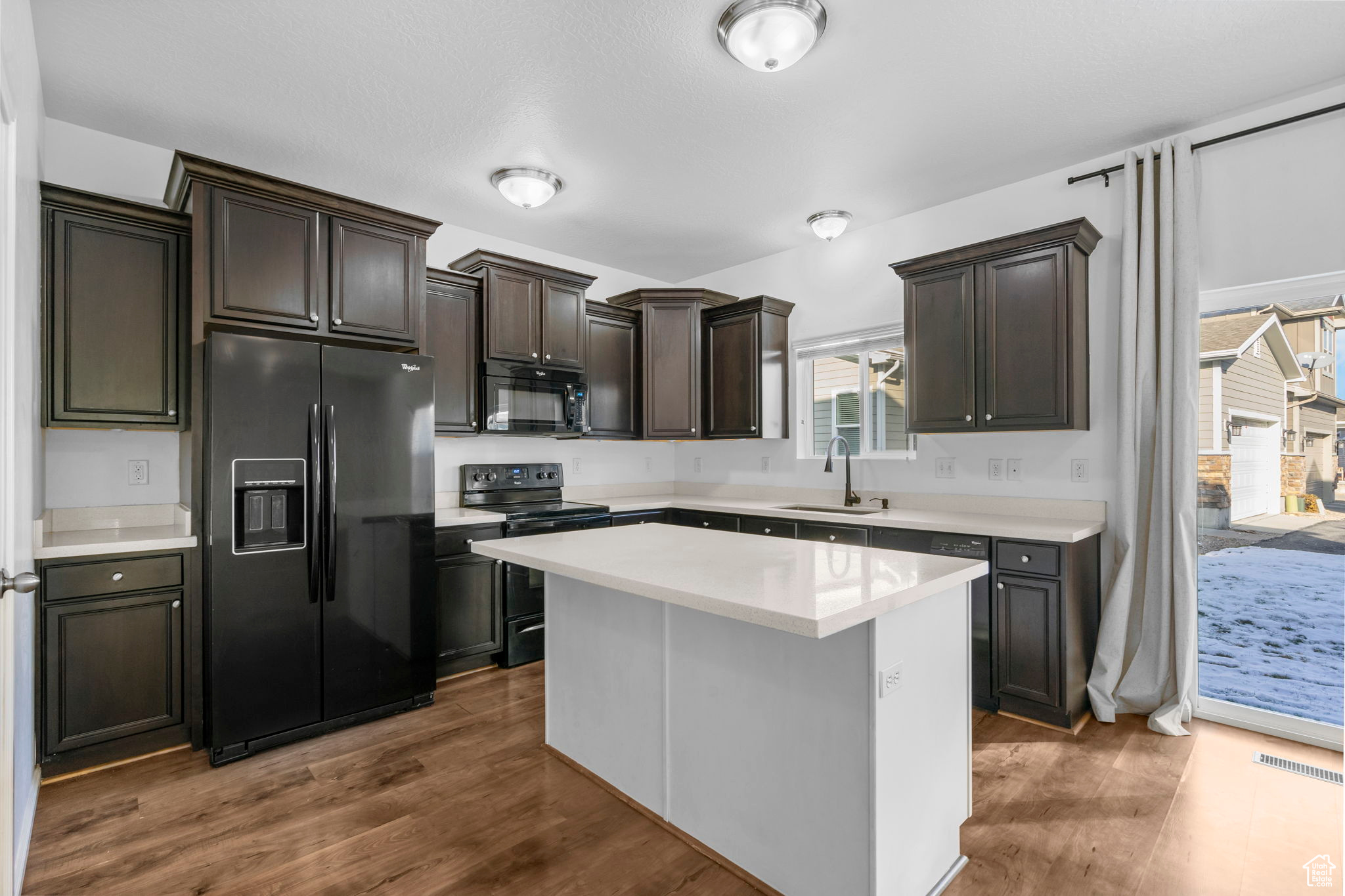 Kitchen featuring black appliances, a center island, dark hardwood / wood-style flooring, and sink