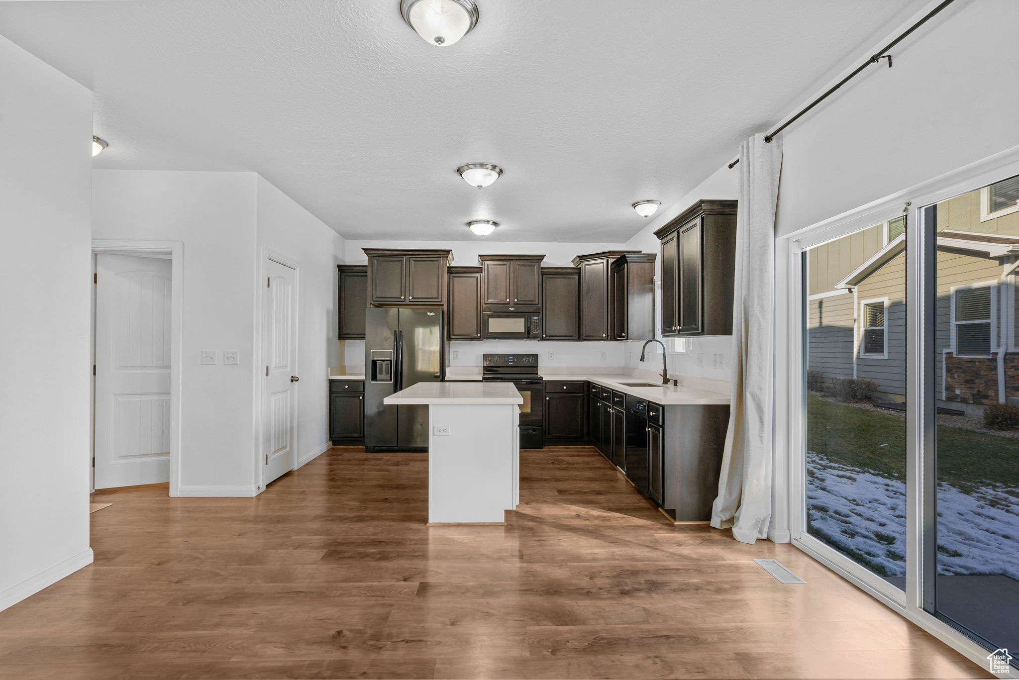 Kitchen with dark hardwood / wood-style flooring, a center island, black appliances, and sink