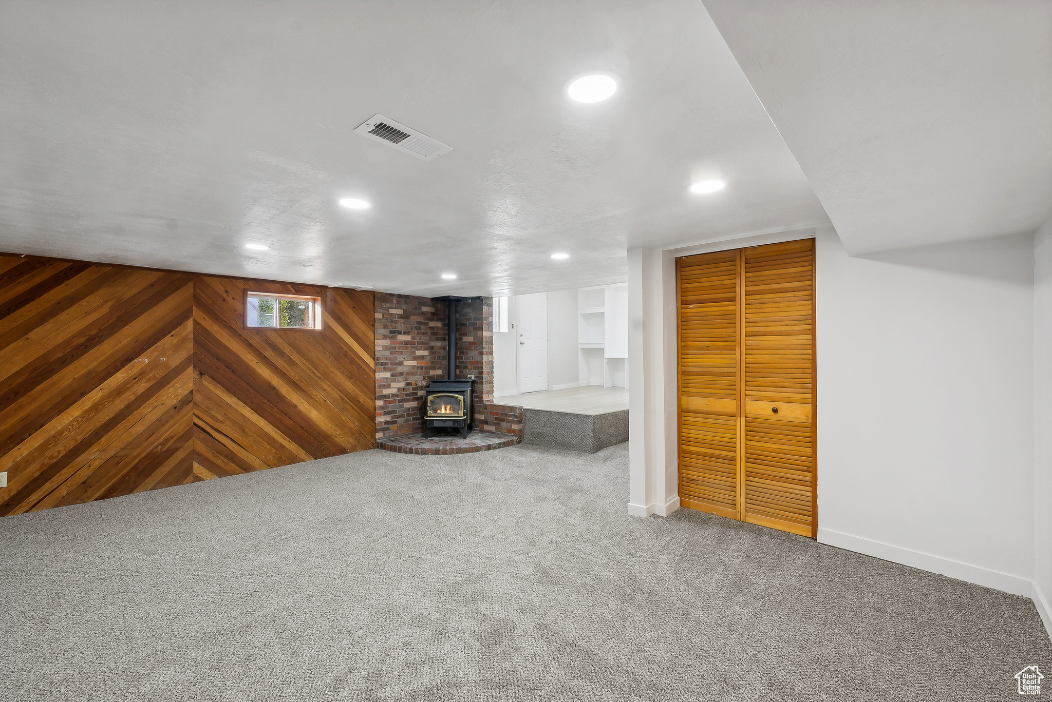 Unfurnished living room featuring carpet, a gas stove, and wooden walls