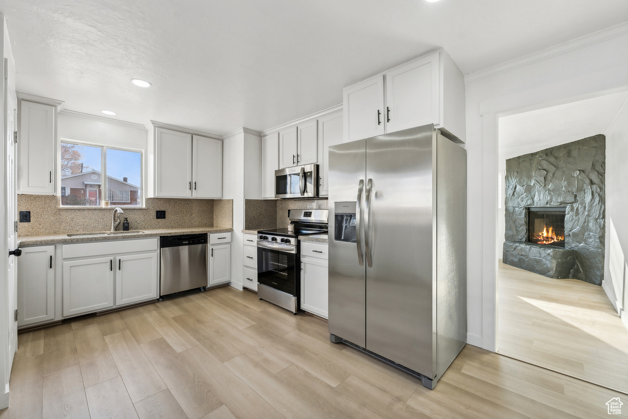 Kitchen with stainless steel appliances, white cabinetry, and light hardwood / wood-style flooring