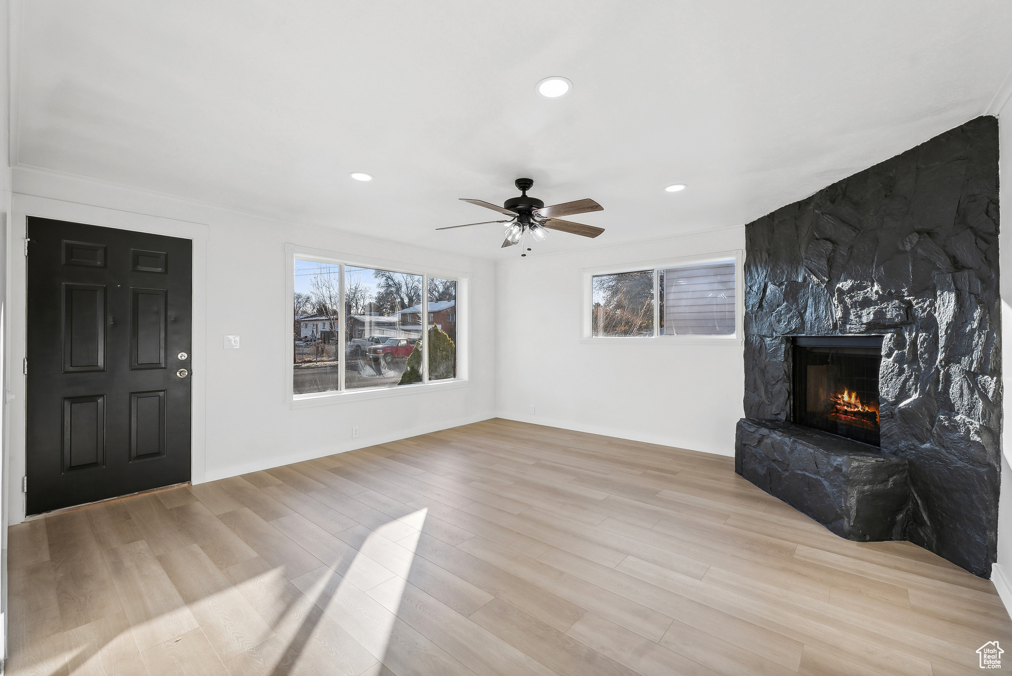 Unfurnished living room featuring ceiling fan, a fireplace, and light hardwood / wood-style flooring