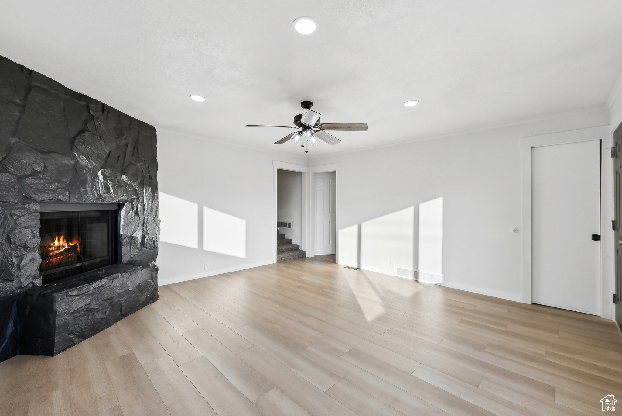 Unfurnished living room featuring ceiling fan, ornamental molding, a fireplace, and light hardwood / wood-style flooring