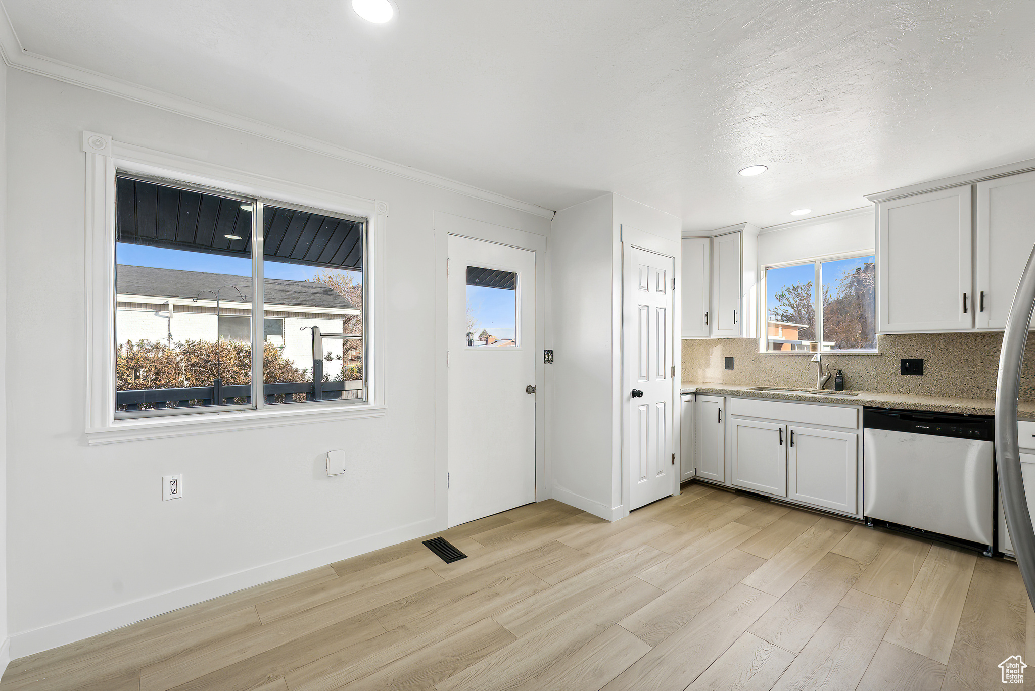 Kitchen featuring dishwasher, sink, tasteful backsplash, light hardwood / wood-style floors, and white cabinetry