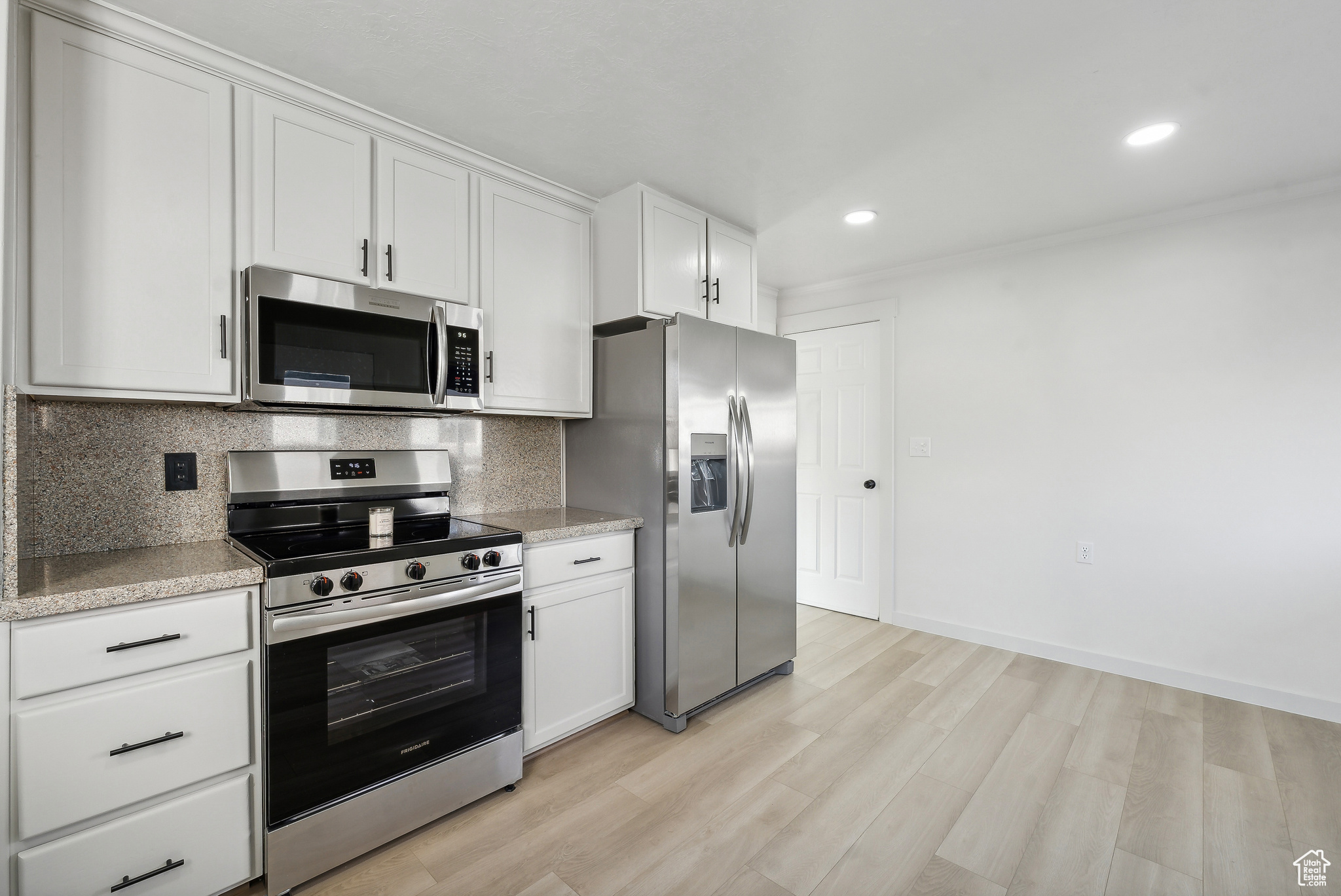 Kitchen featuring white cabinets, appliances with stainless steel finishes, decorative backsplash, and light hardwood / wood-style flooring