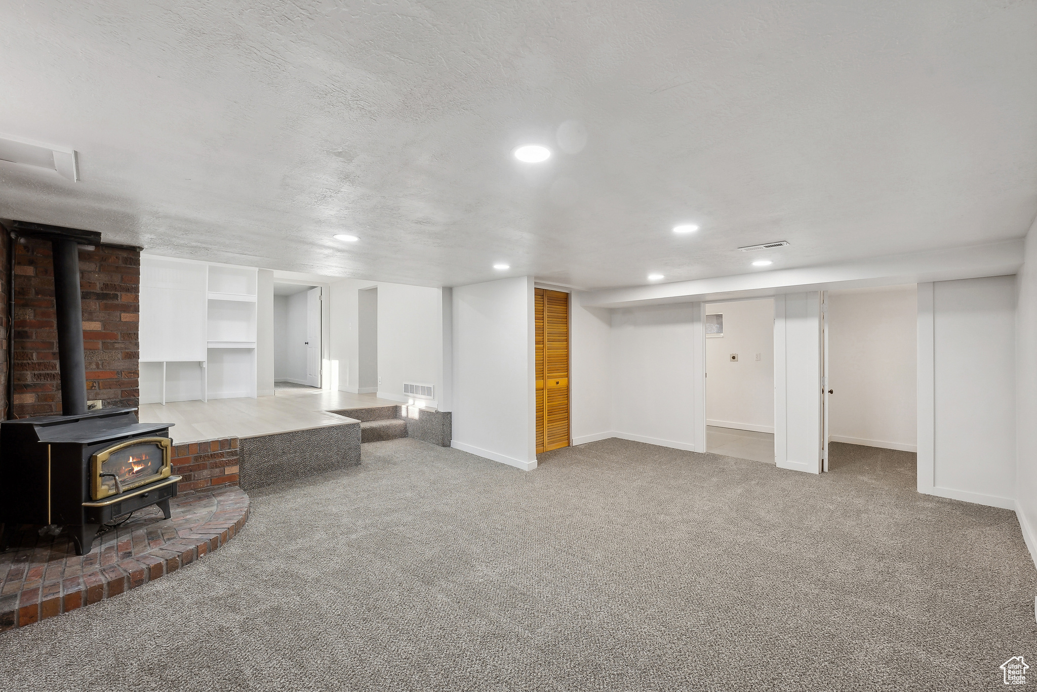 Basement with light carpet, a textured ceiling, and a wood stove