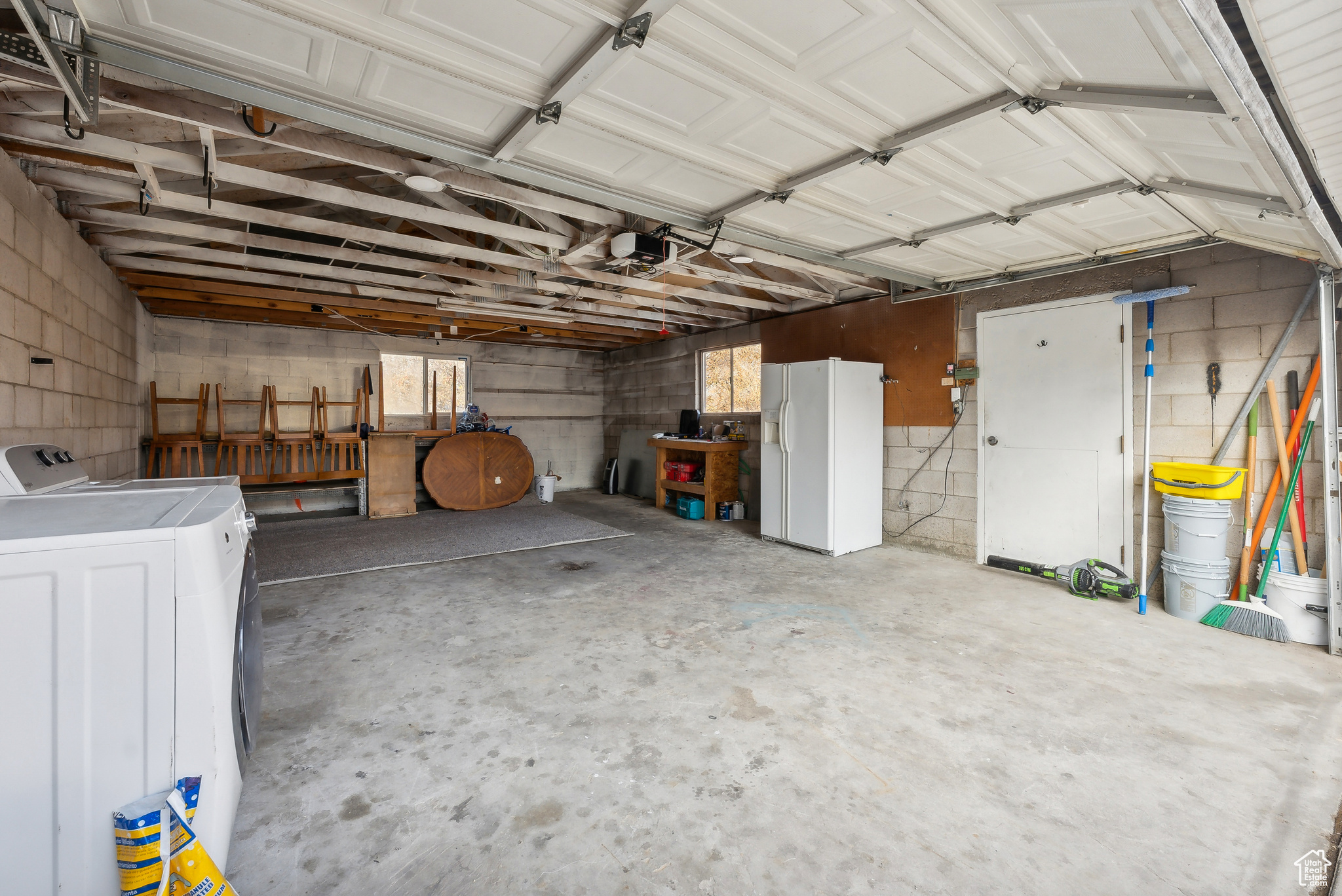 Garage featuring independent washer and dryer, white refrigerator with ice dispenser, and a garage door opener