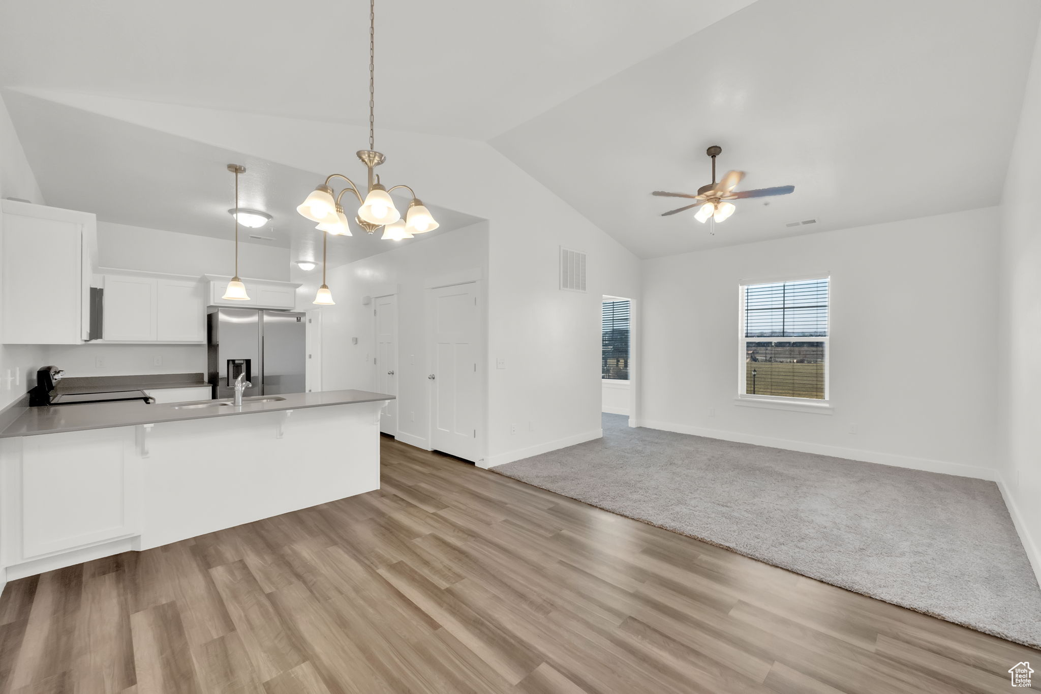 Kitchen featuring light LVP flooring, stainless steel fridge, pendant lighting, vaulted ceiling, and white cabinets