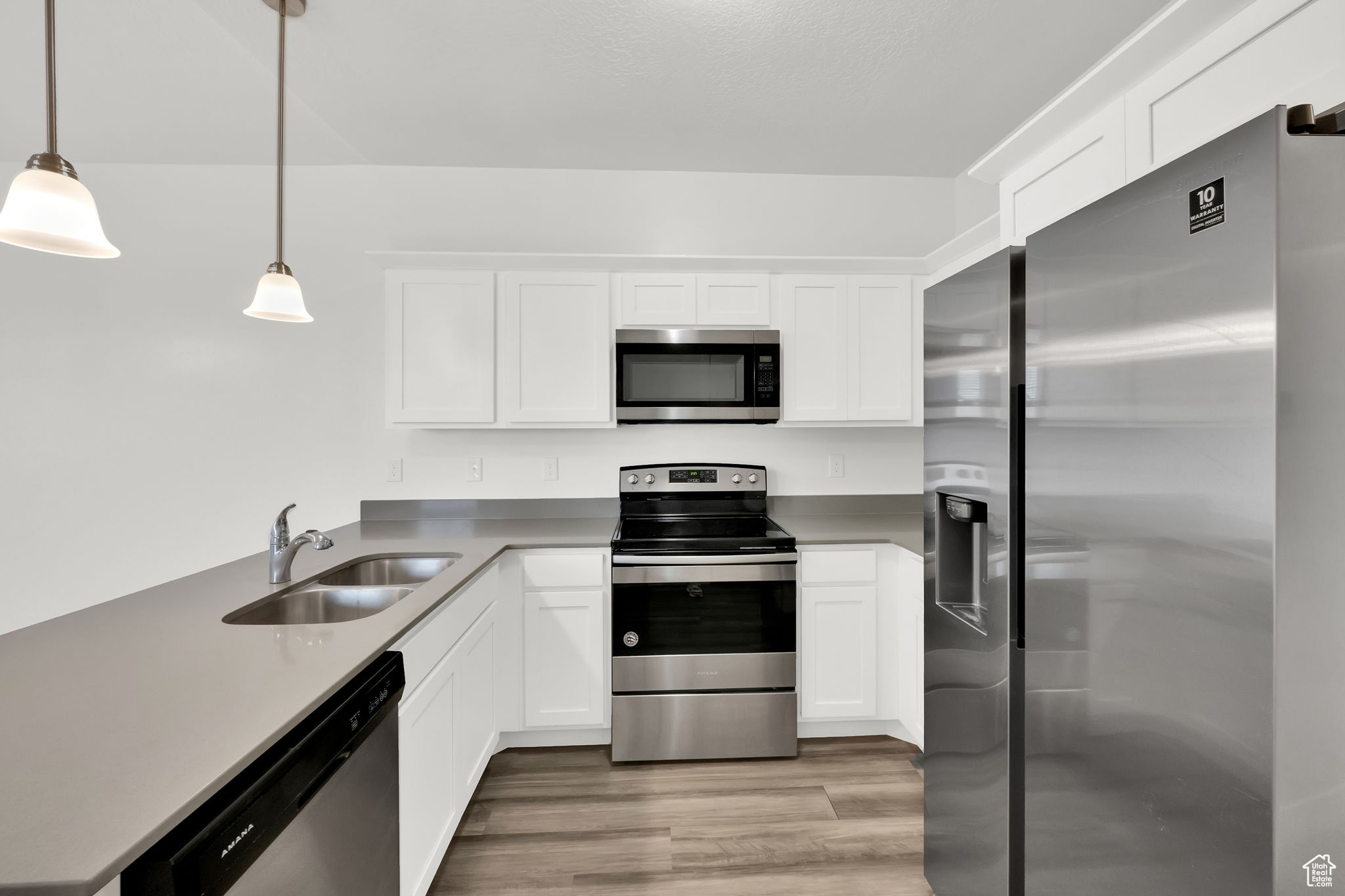 Kitchen featuring sink, stainless steel appliances, light LVP flooring, decorative light fixtures, and white cabinets