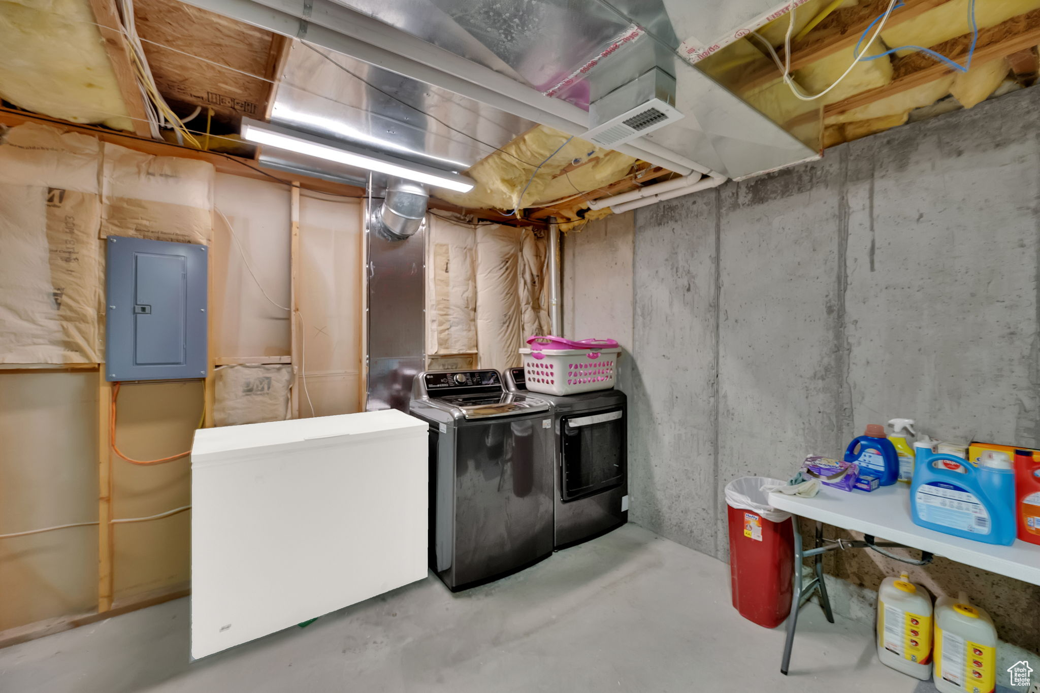 Basement featuring washing machine and clothes dryer, electric panel, and refrigerator