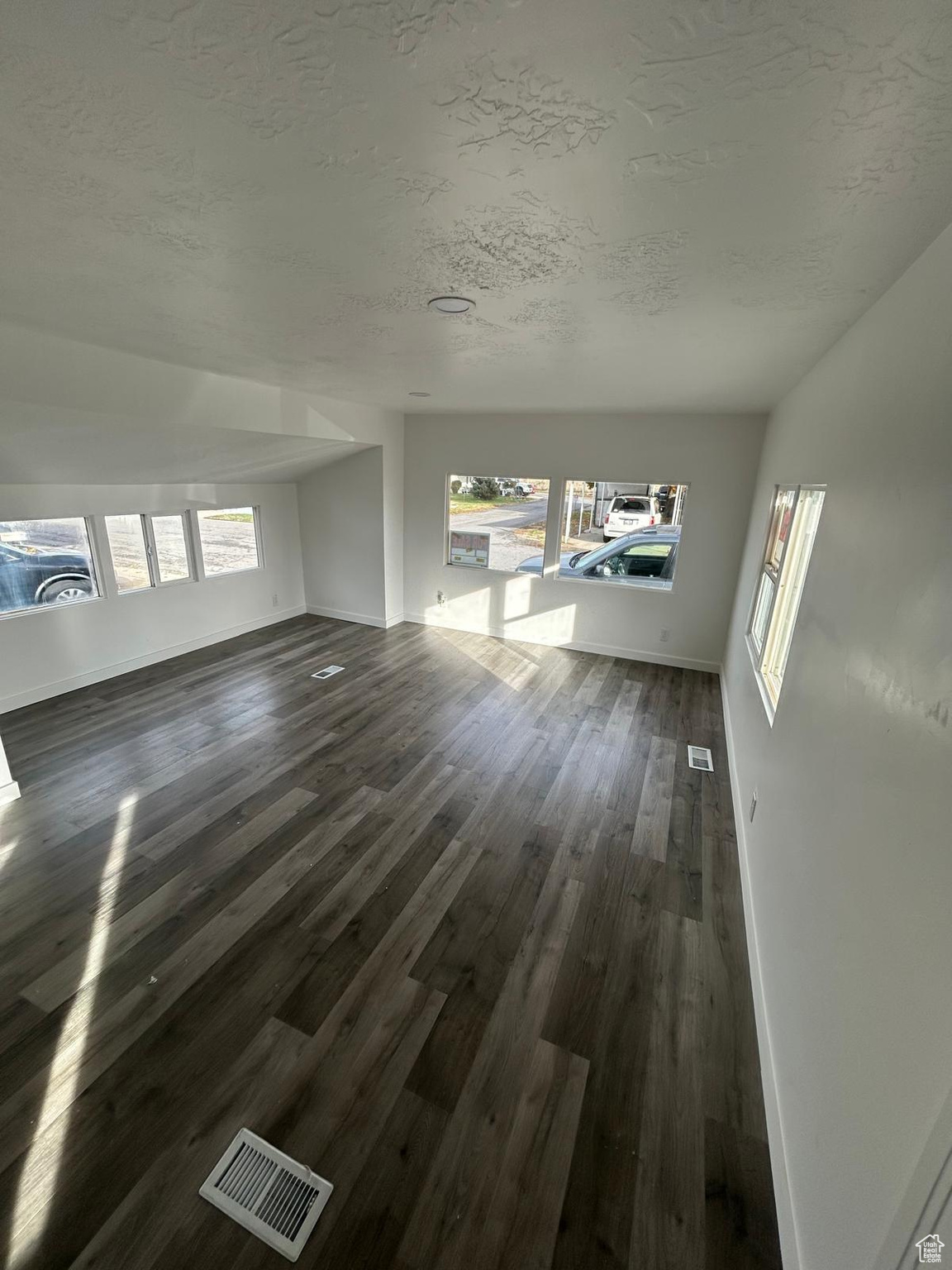 Unfurnished living room featuring dark hardwood / wood-style flooring and a textured ceiling