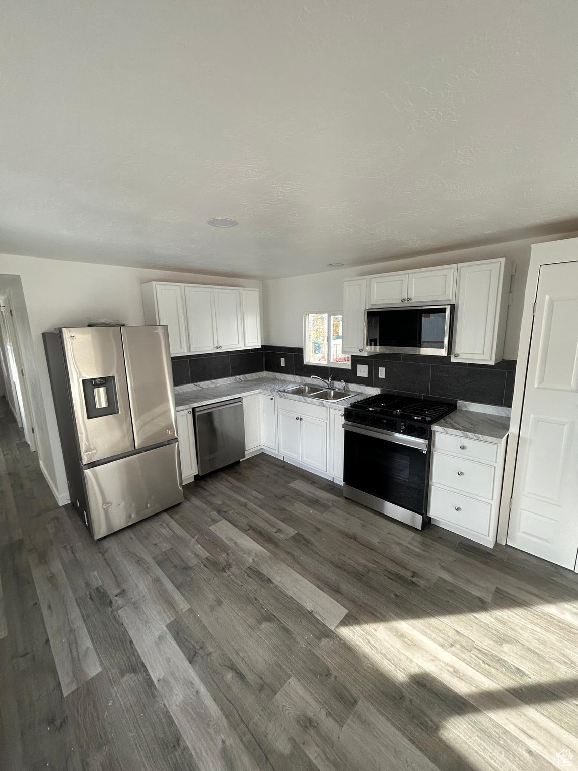 Kitchen featuring decorative backsplash, stainless steel appliances, dark wood-type flooring, sink, and white cabinets