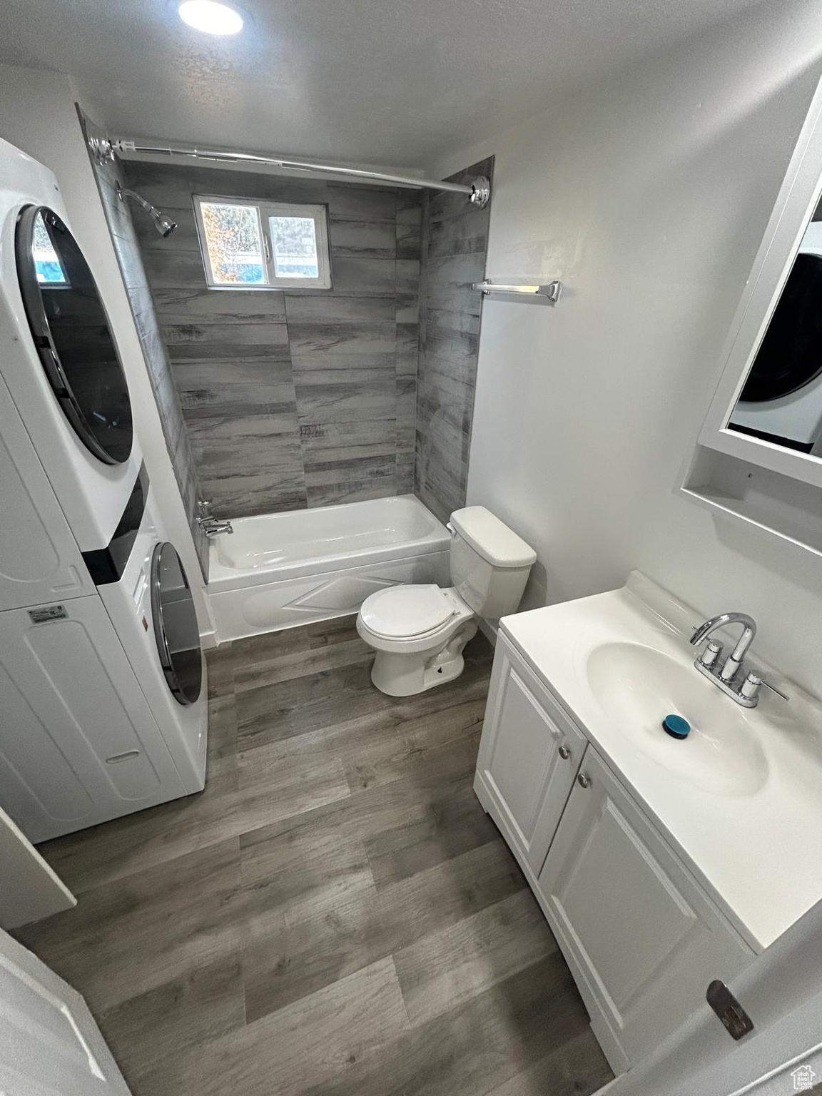 Full bathroom with wood-type flooring, vanity, stacked washer and dryer, and toilet