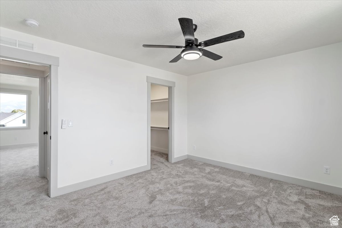 Unfurnished bedroom featuring a walk in closet, ceiling fan, a closet, and light carpet