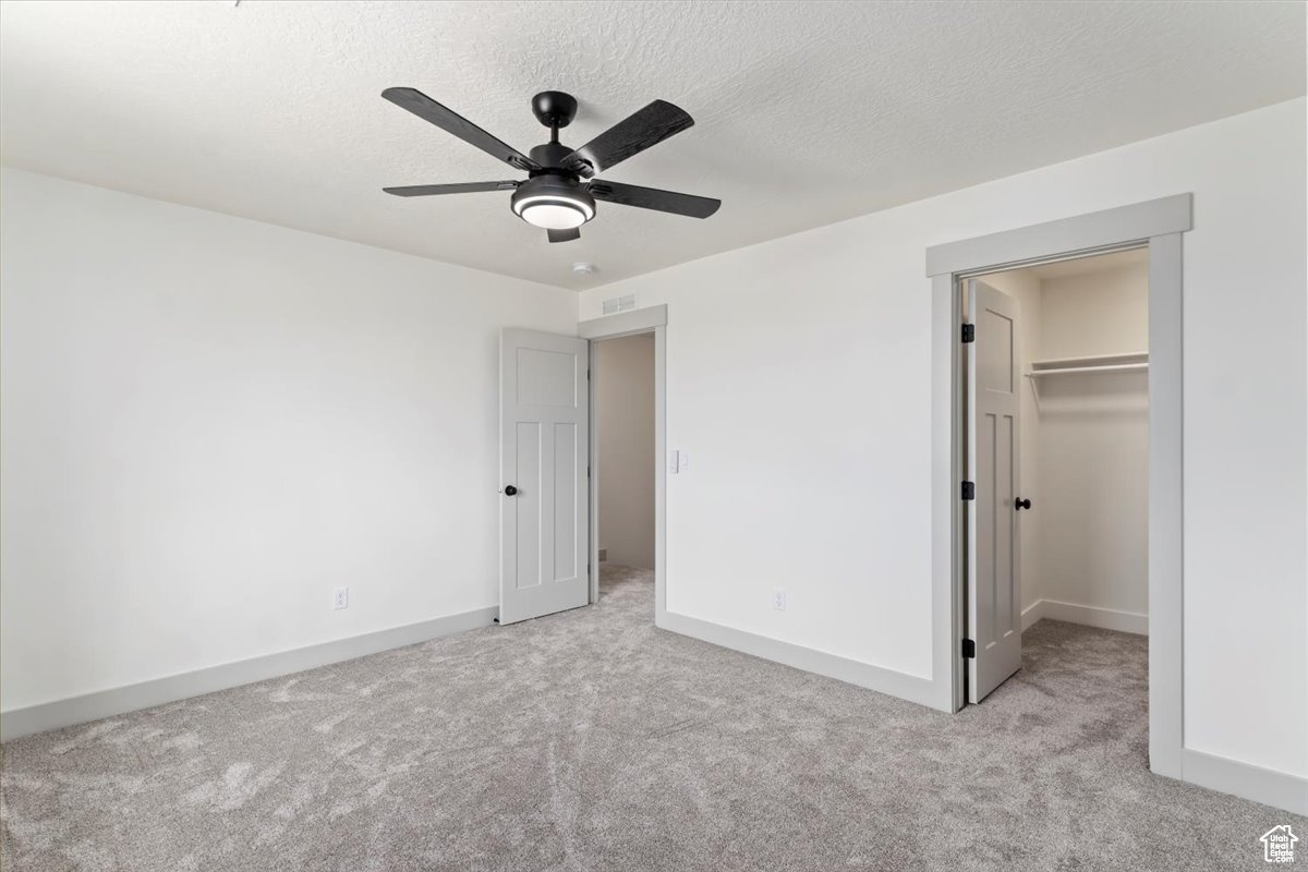 Unfurnished bedroom with a spacious closet, ceiling fan, light colored carpet, a textured ceiling, and a closet