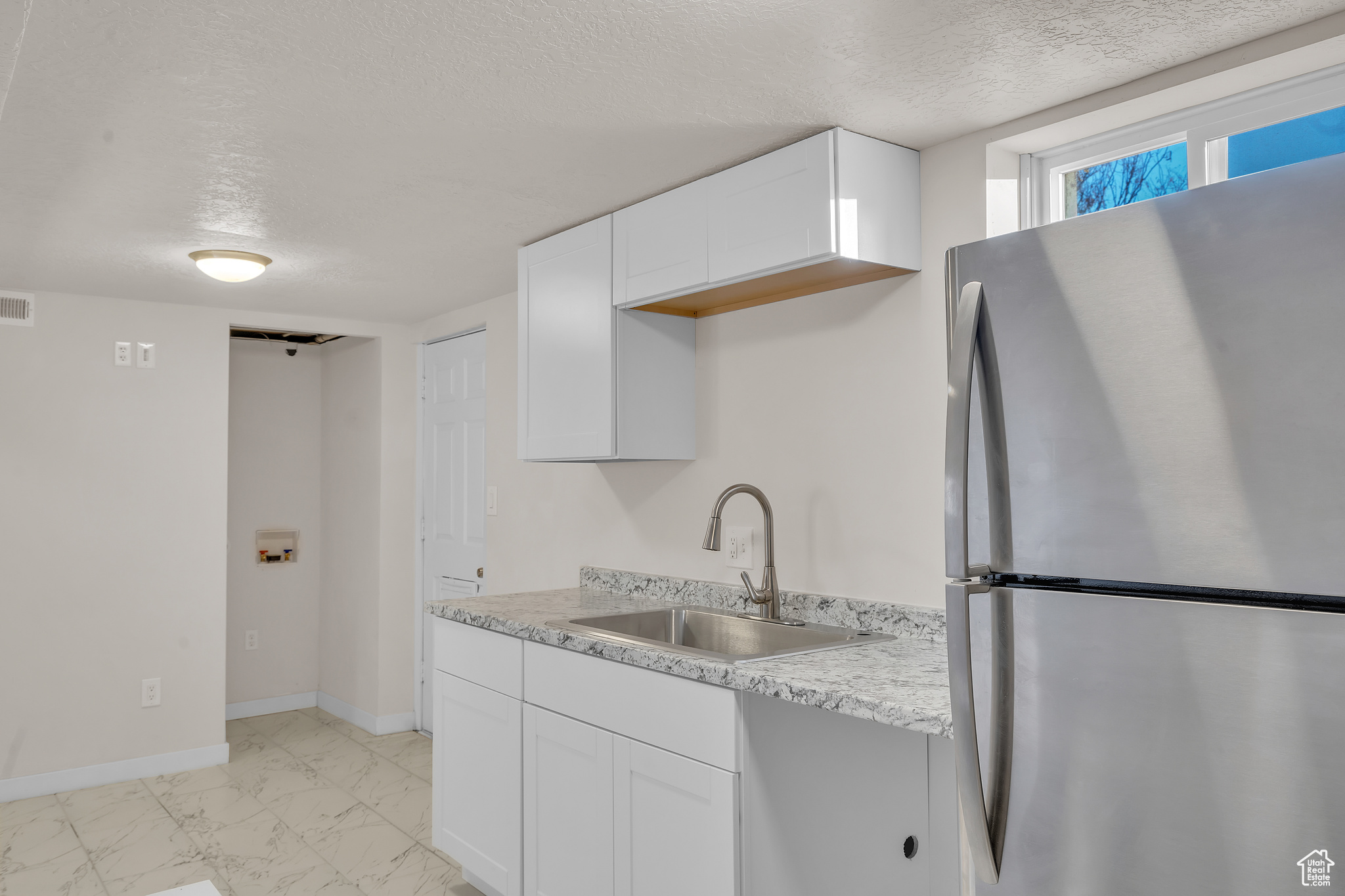 Kitchen with stainless steel refrigerator, sink, white cabinets, and a textured ceiling