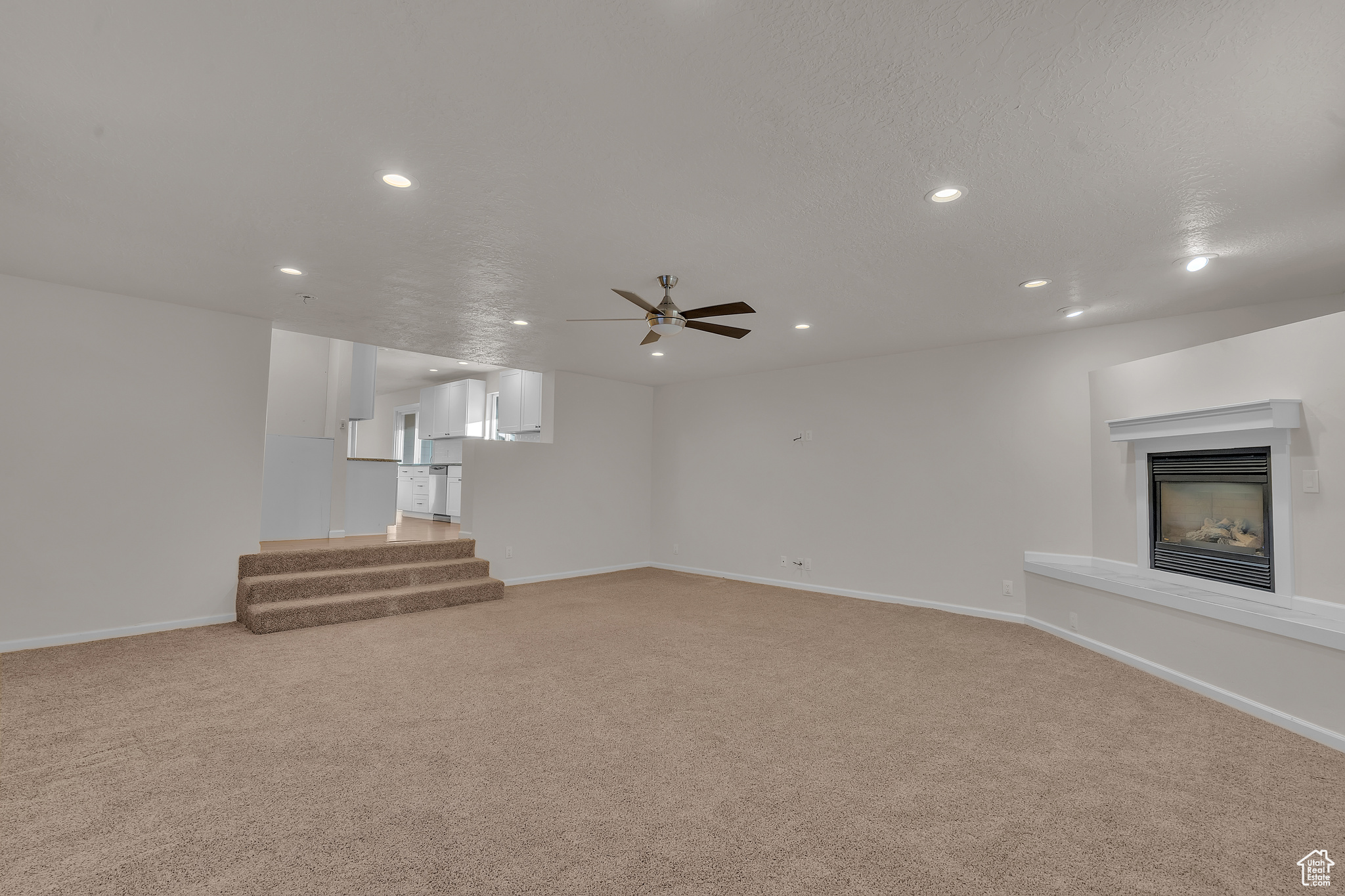 Unfurnished living room with a textured ceiling, ceiling fan, and light carpet