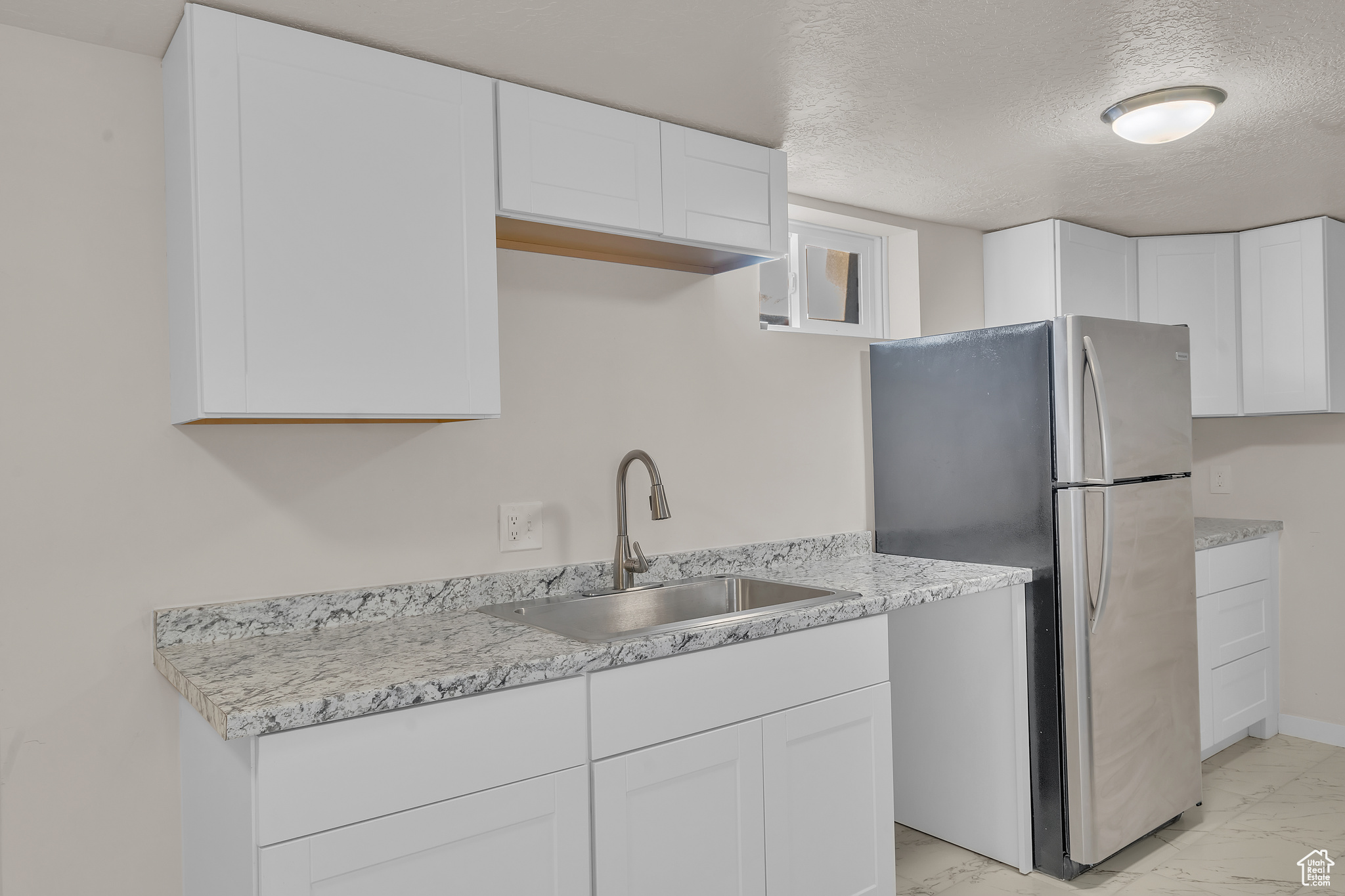 Kitchen with white cabinets, a textured ceiling, stainless steel refrigerator, and sink