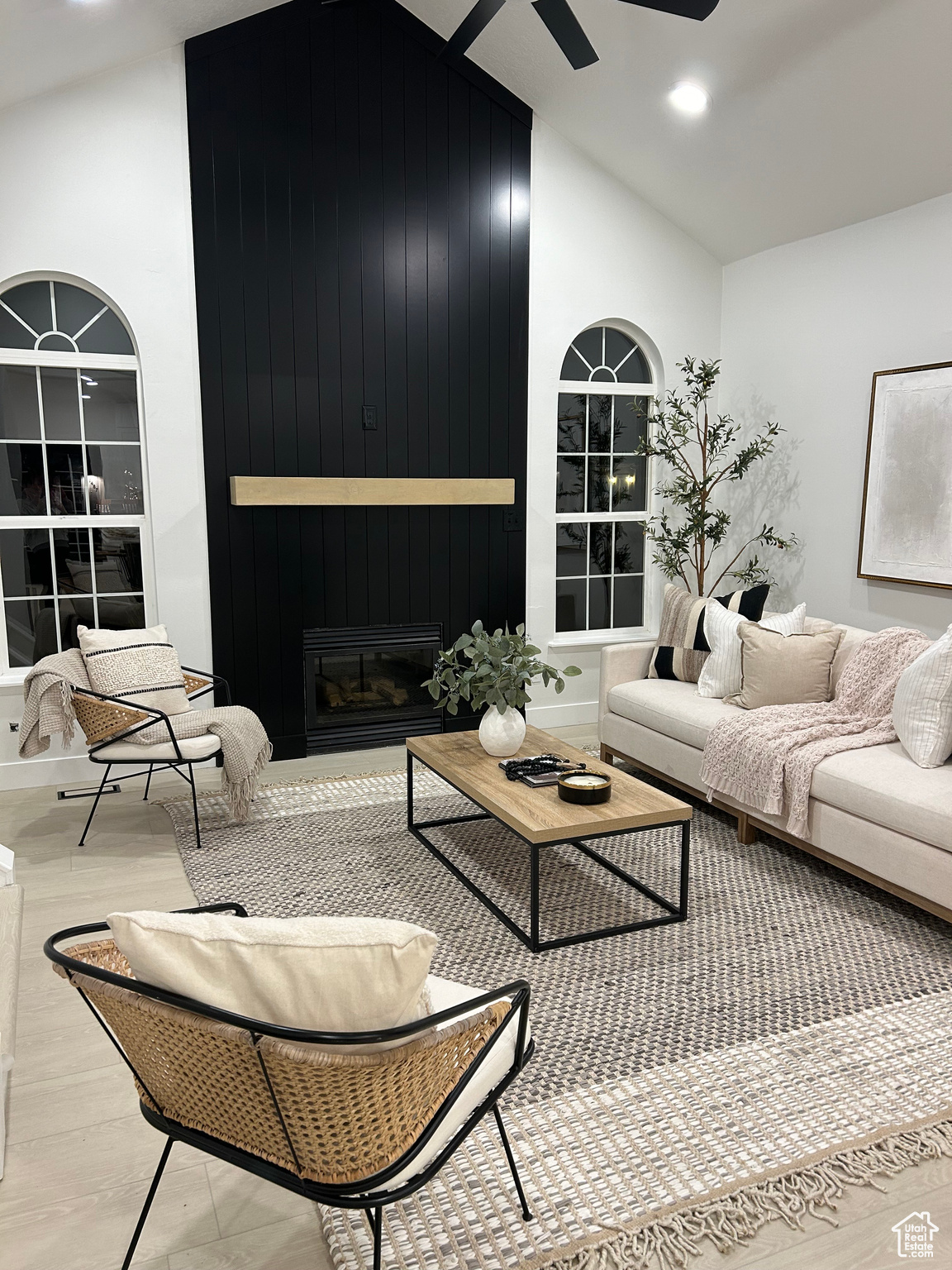 Living room featuring high vaulted ceiling, wooden walls, ceiling fan, light hardwood / wood-style floors, and a large fireplace