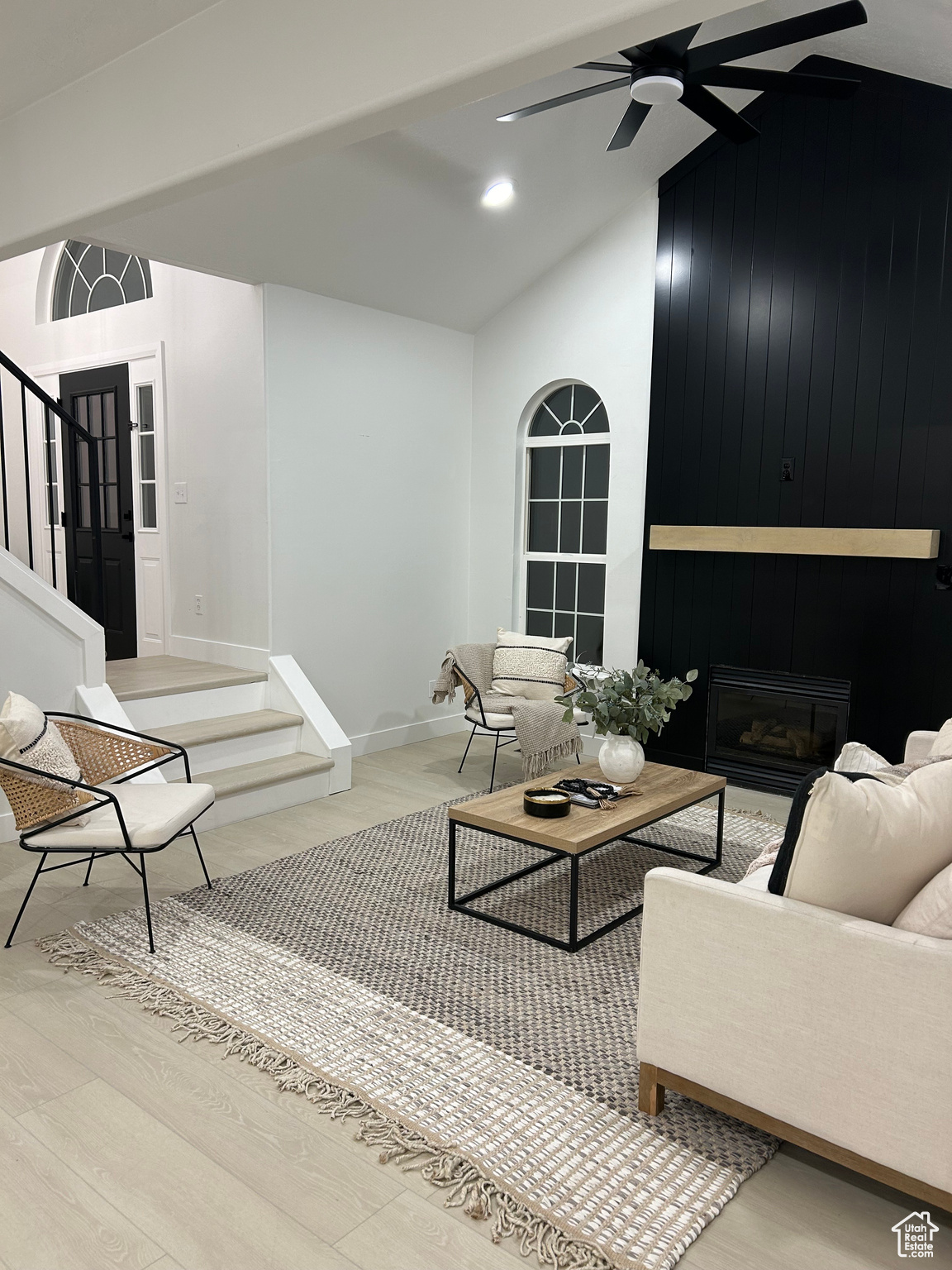 Living room with a large fireplace, ceiling fan, light hardwood / wood-style flooring, lofted ceiling, and wood walls